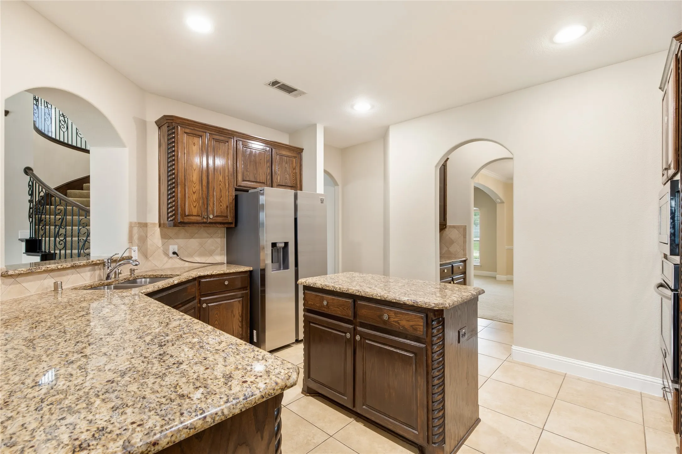 Kitchen featuring granite countertops, wood cabinetry, stainless steel refrigerator, and integrated double ovens