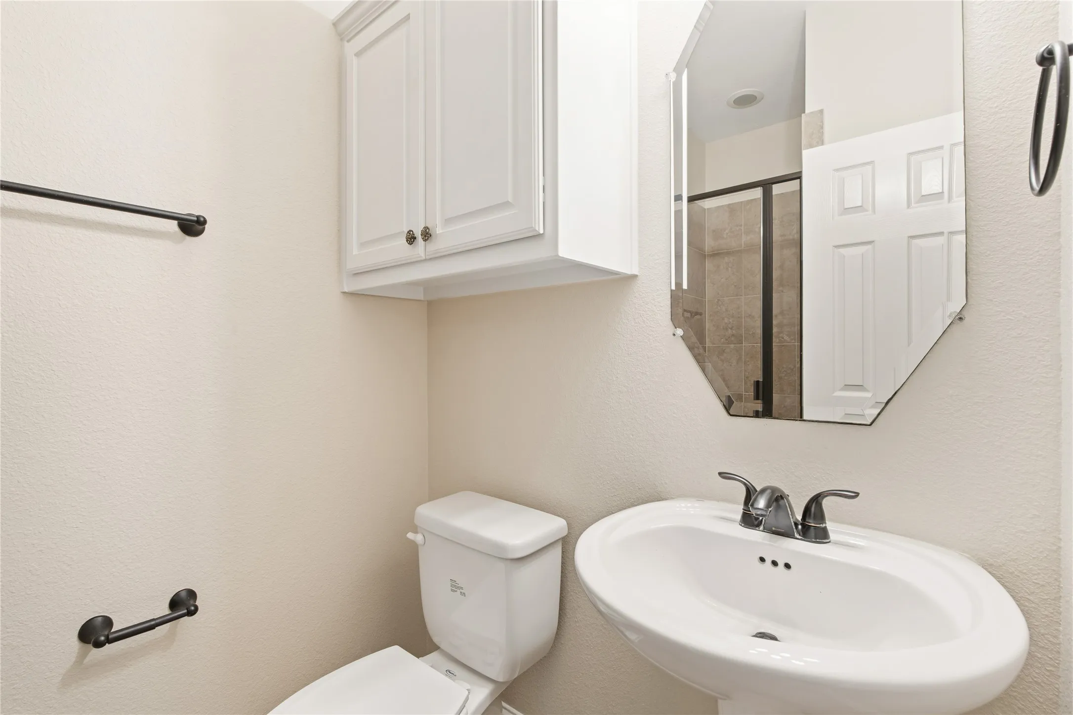 Pedestal sink with dark-finished faucet, complemented by a decorative octagonal mirror