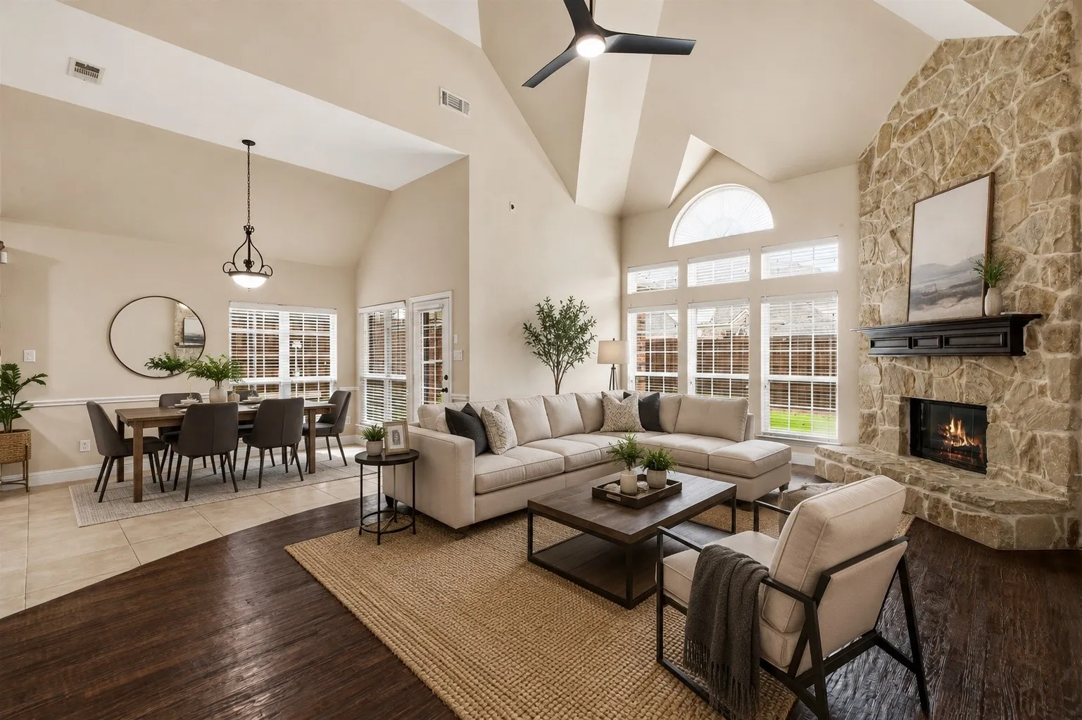Virtually Staged Vaulted ceiling living area featuring a stone fireplace, wood-finish flooring, large windows, and a dining area with tile flooring