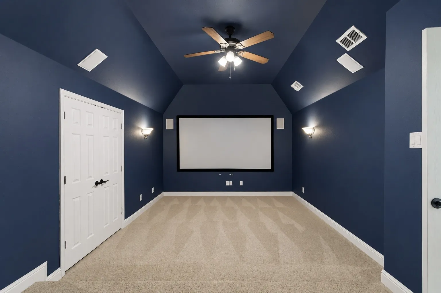 Dedicated media room featuring a large projection screen, two sconce lights, and a ceiling fan with integrated lighting