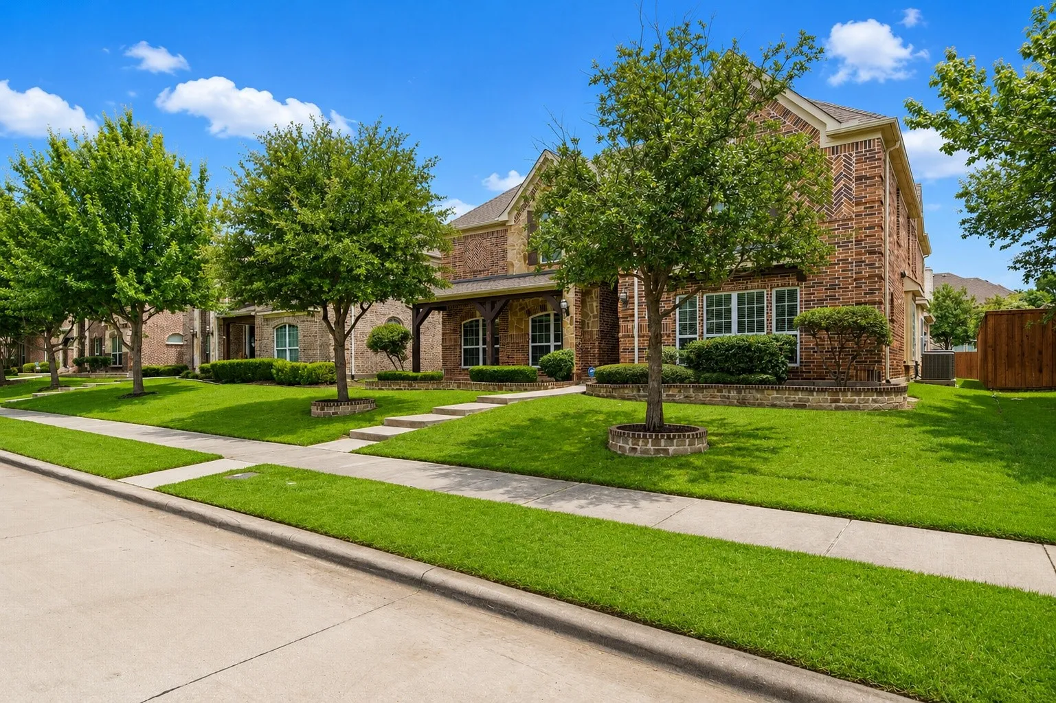 Brick exterior with stone accents, covered porch entry, multiple windows, established trees, and a concrete sidewalk