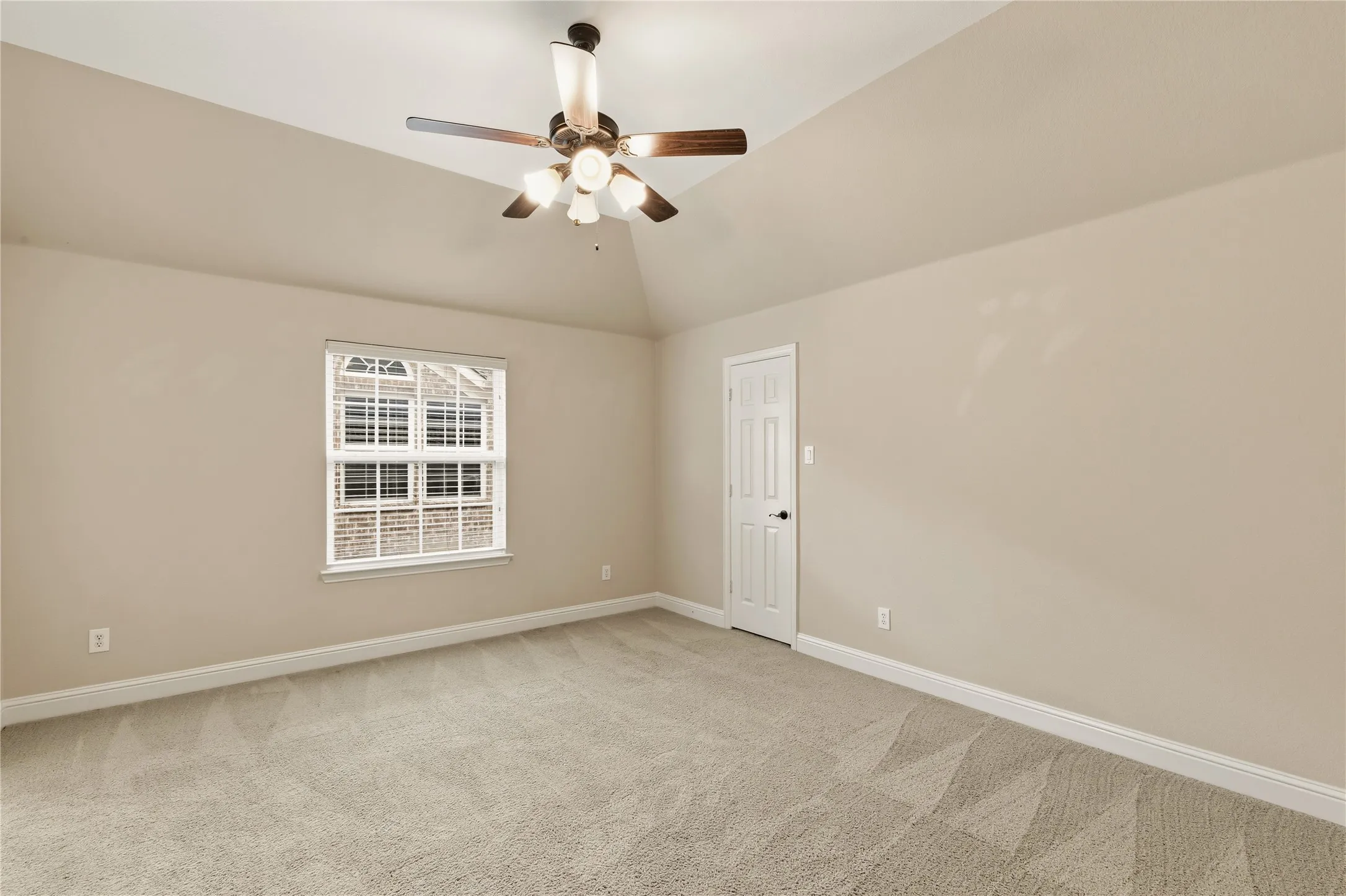 Vaulted ceiling room featuring light beige carpeting, a window with white louvered blinds, and a ceiling fan with integrated lighting