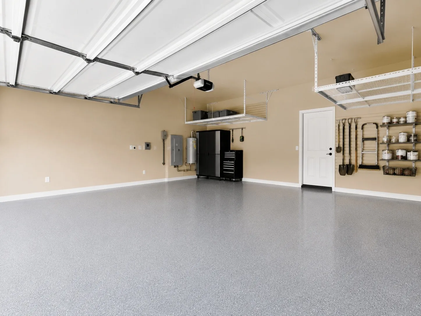 Spacious garage featuring a durable epoxy-coated floor, overhead storage racks, a white paneled door, and built-in wall organization systems