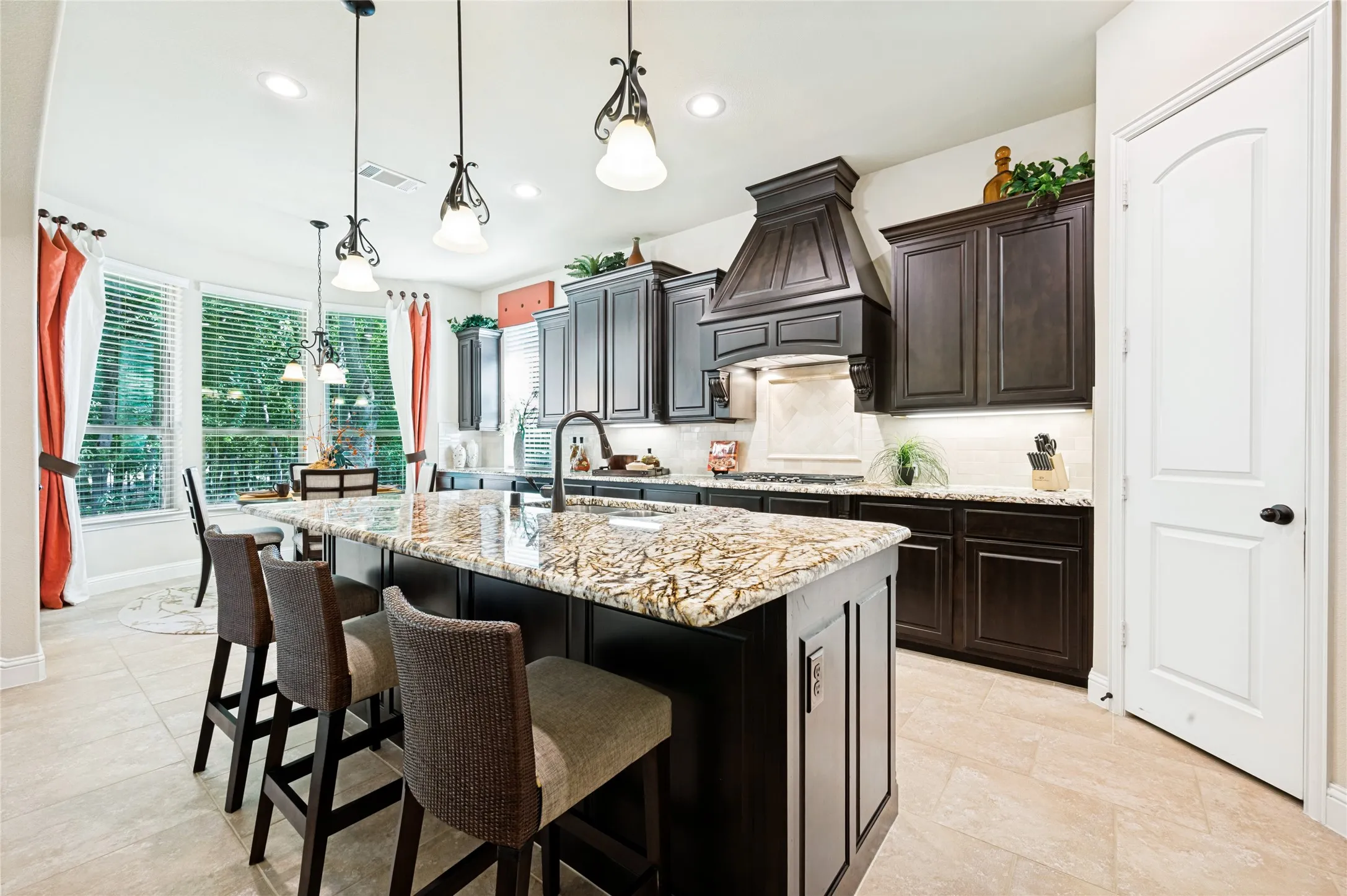 The gourmet kitchen features an open concept layout seamlessly flowing into the family room, complete with a central island, granite countertops, an integrated sink, custom wood cabinetry, a decorative range hood, recessed and pendant lighting, and a spacious walk-in pantry.
