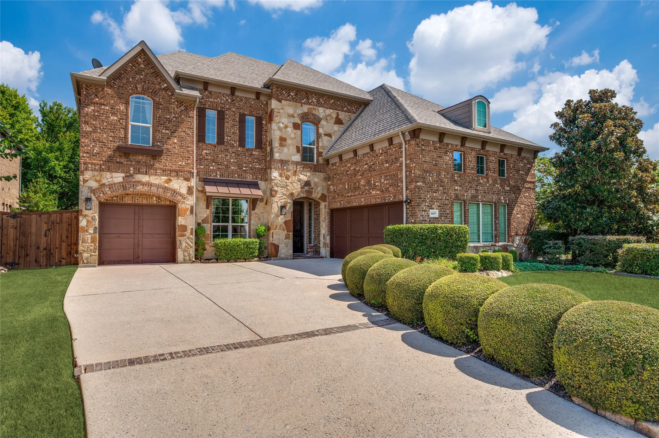 This former model home boasts professional custom landscaping, an expansive creek-side corner lot, and a sophisticated brick and stone facade, complemented by a spacious three-car garage with cedar-clad doors.