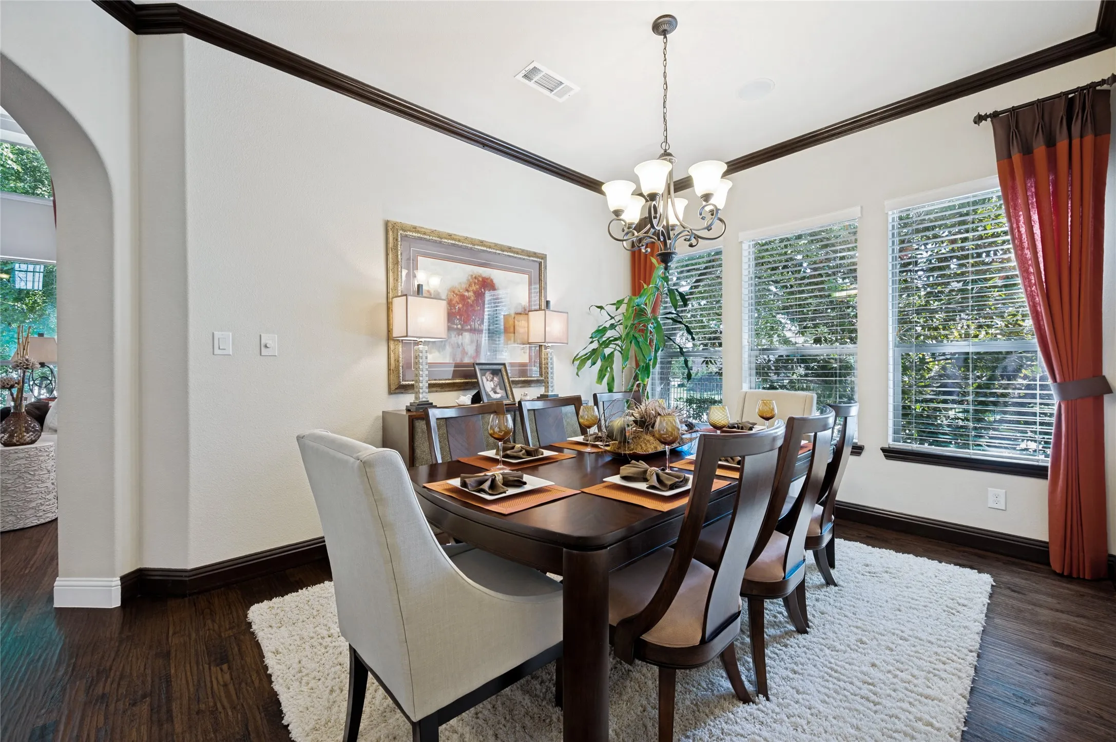This spacious formal dining area features hand-scraped hardwood flooring, an arched entryway, a designer chandelier, and an abundance of natural light provided by multiple windows.