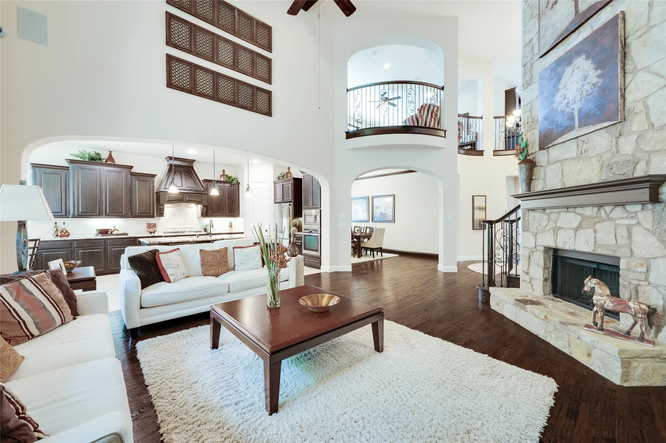 Expansive open-concept design featuring wood-finish flooring, a stone-clad fireplace with mantel, and an arched entryway to the kitchen