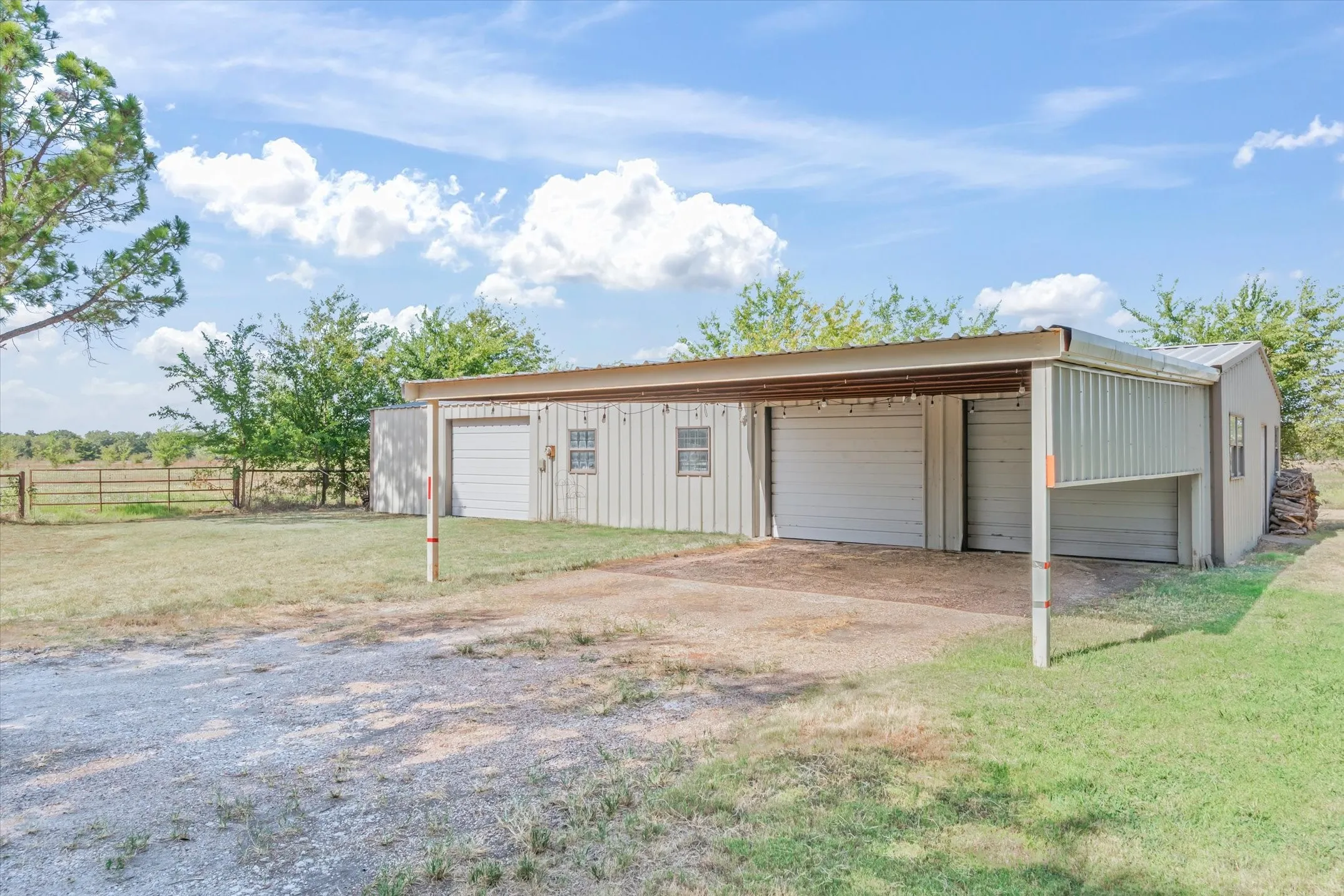 Metal outbuilding with two garage doors, an attached carport, and multiple windows