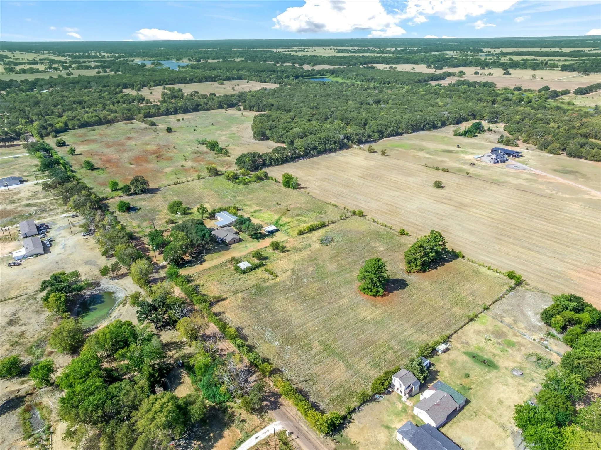 Expansive rural landscape featuring a mix of open fields, wooded areas, and scattered residential structures