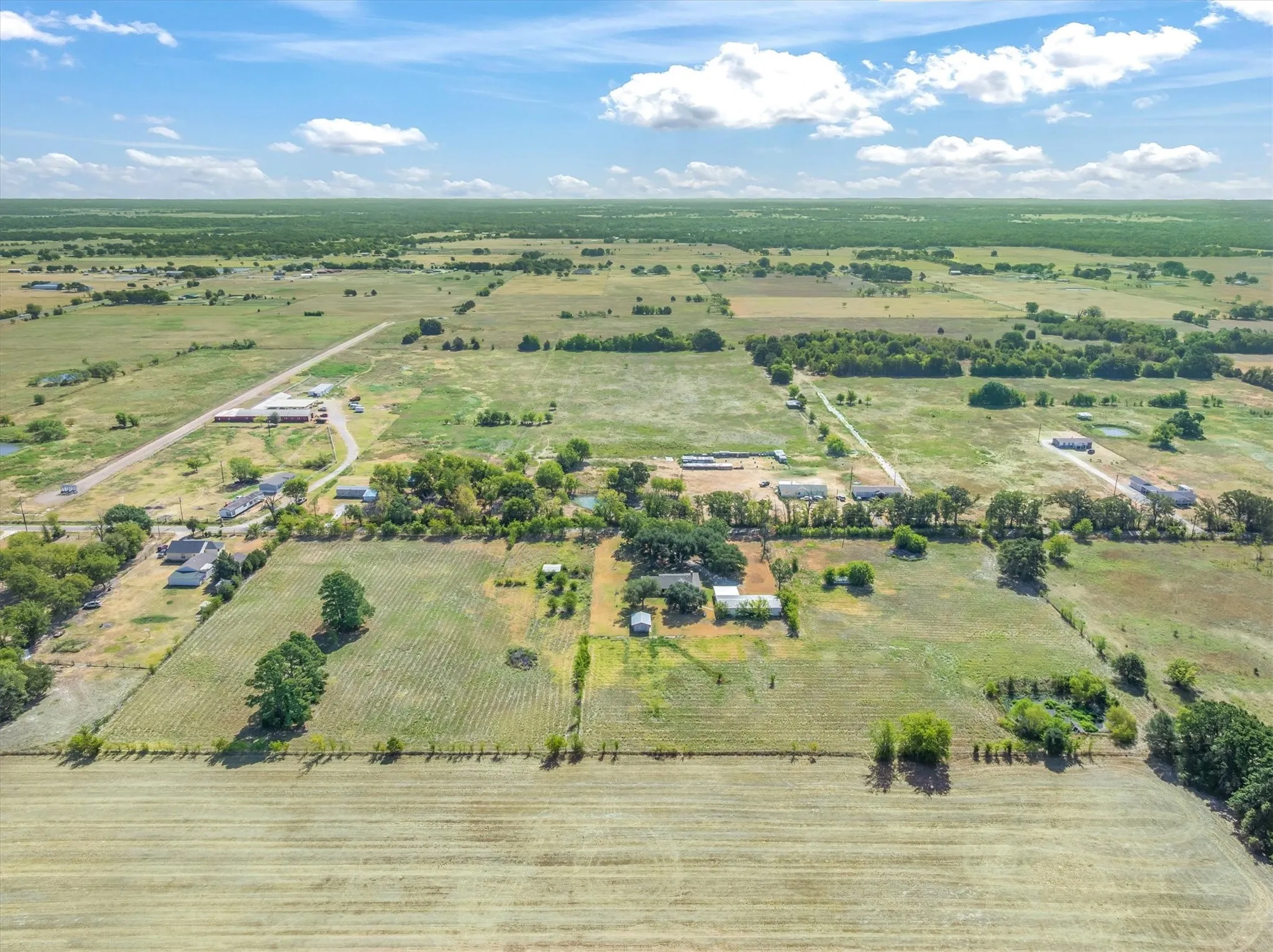 Expansive rural acreage featuring productive agricultural land, mature tree-lined perimeter, established homestead with outbuildings, and direct highway access