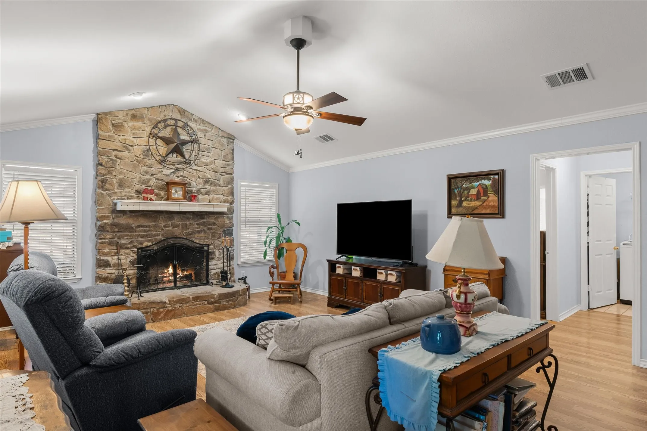 Vaulted ceiling, stone-clad fireplace with mantel, wood-finish flooring, and white trim