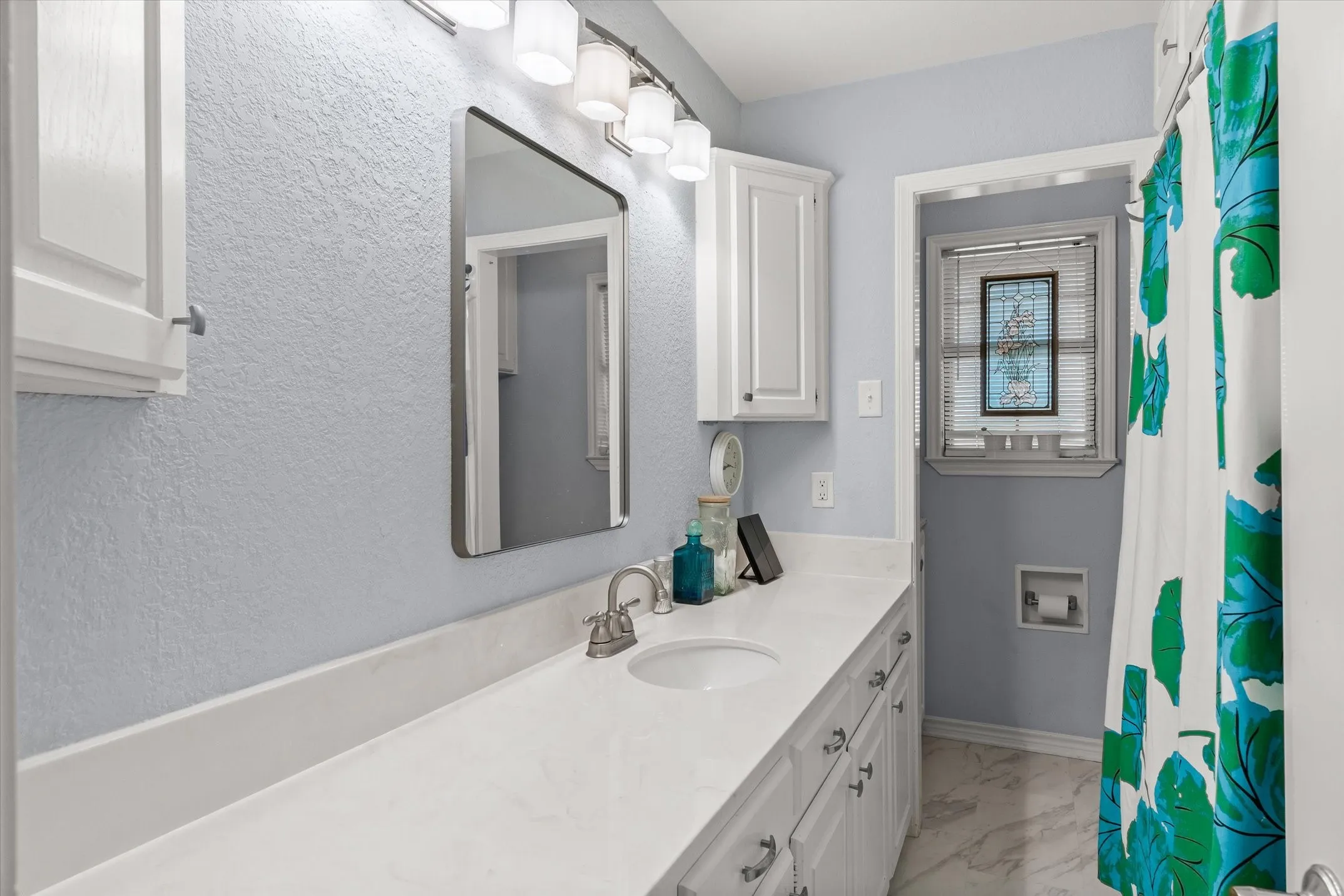 Extended single vanity with undermount sink and brushed nickel faucet, white shaker cabinetry with brushed nickel hardware, and an overhead vanity light bar