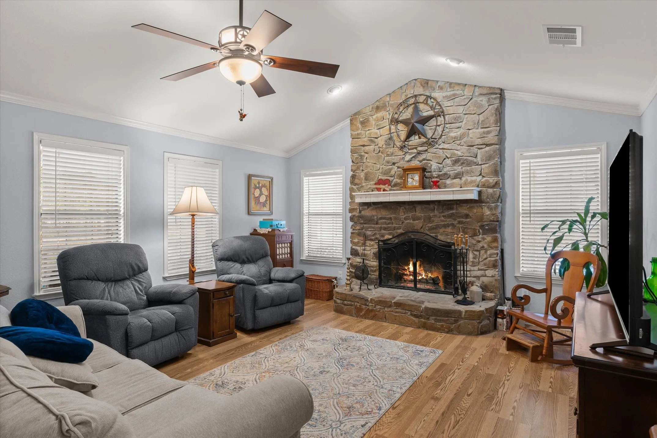Stone-clad fireplace with a hearth, wood-finish flooring, vaulted ceiling, and recessed lighting