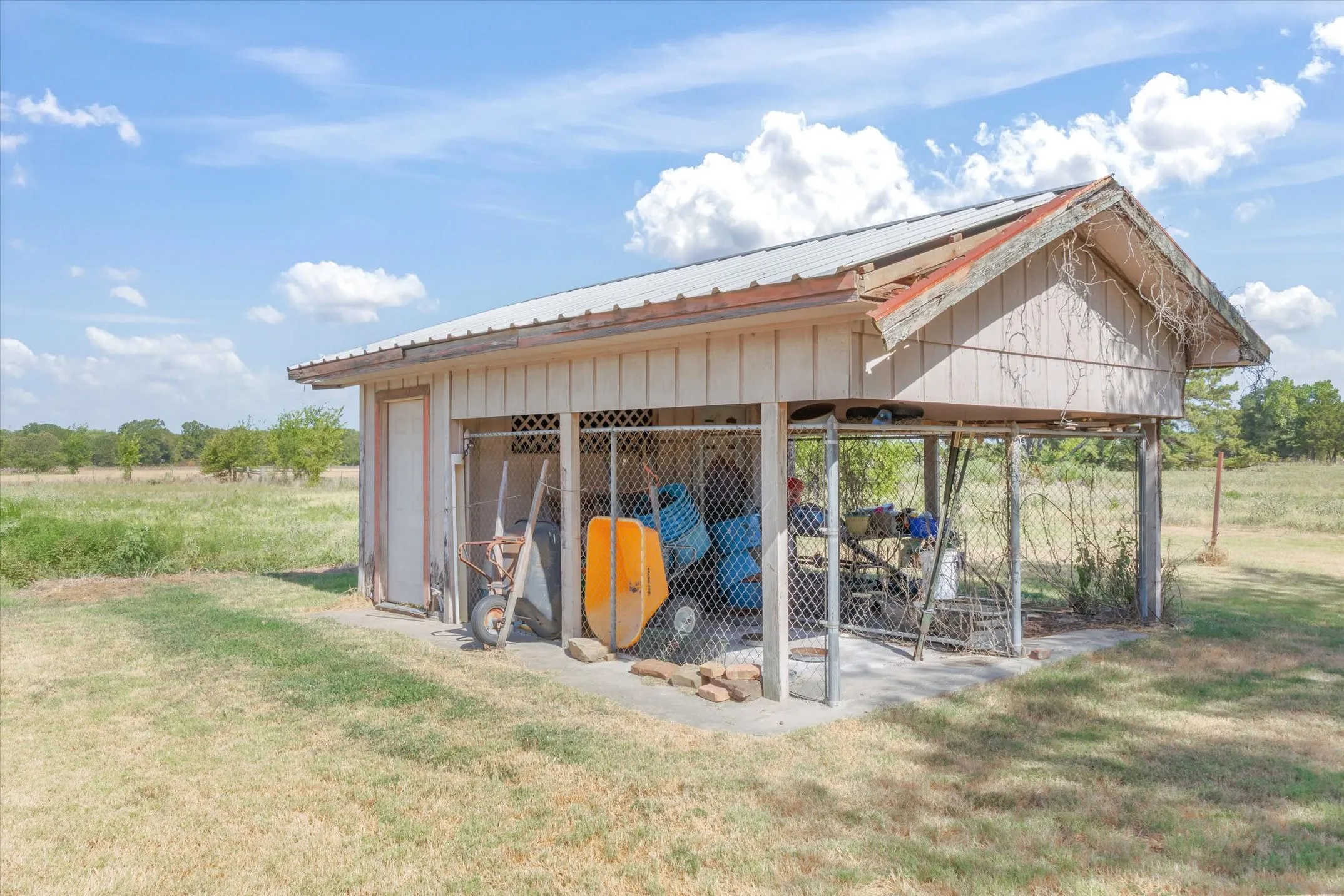 Utility shed with board and batten siding, metal roof, and an attached covered storage area with chain-link fencing