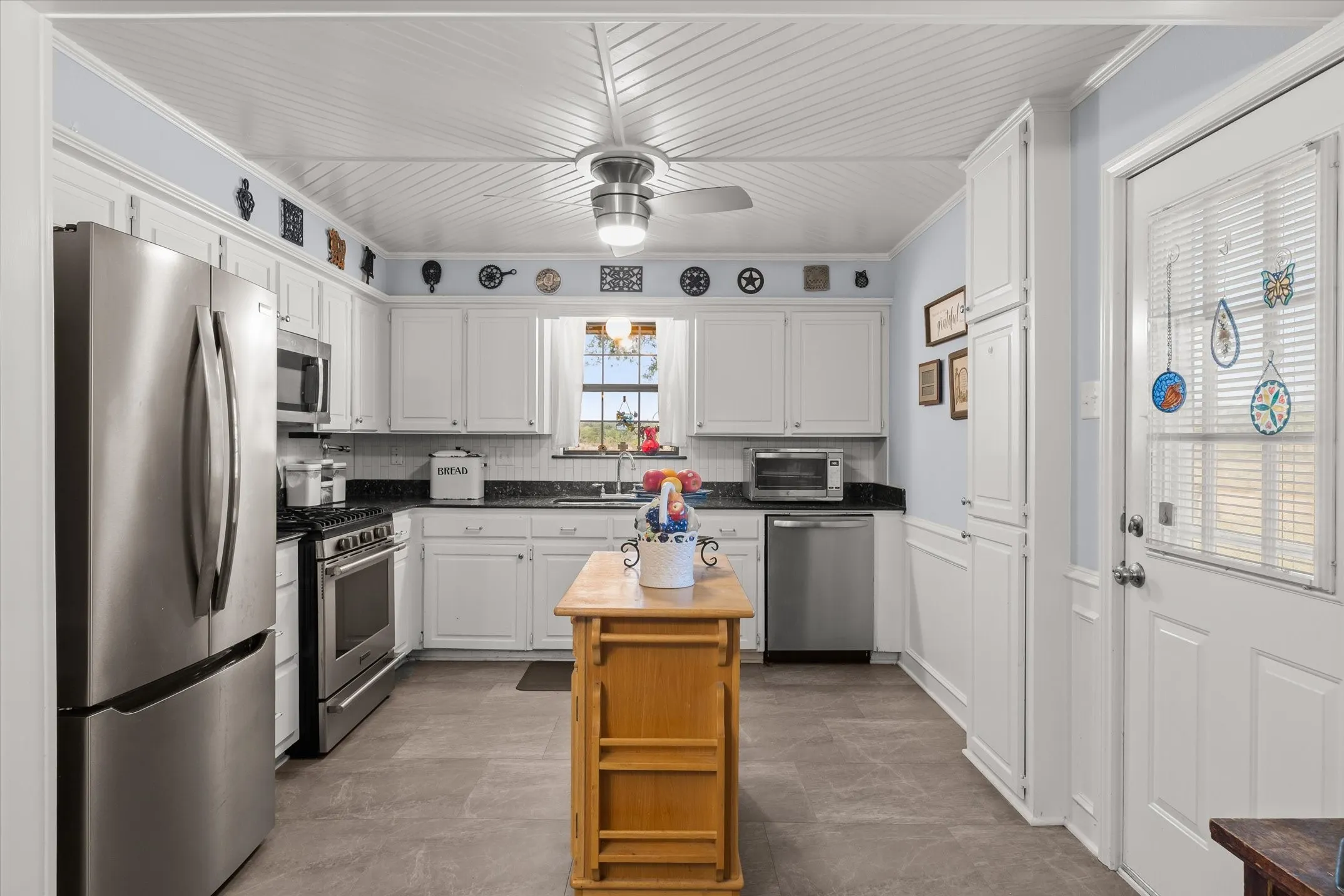 Kitchen featuring white cabinetry, stainless steel appliances, a ceiling fan, and a light wood-finish center island