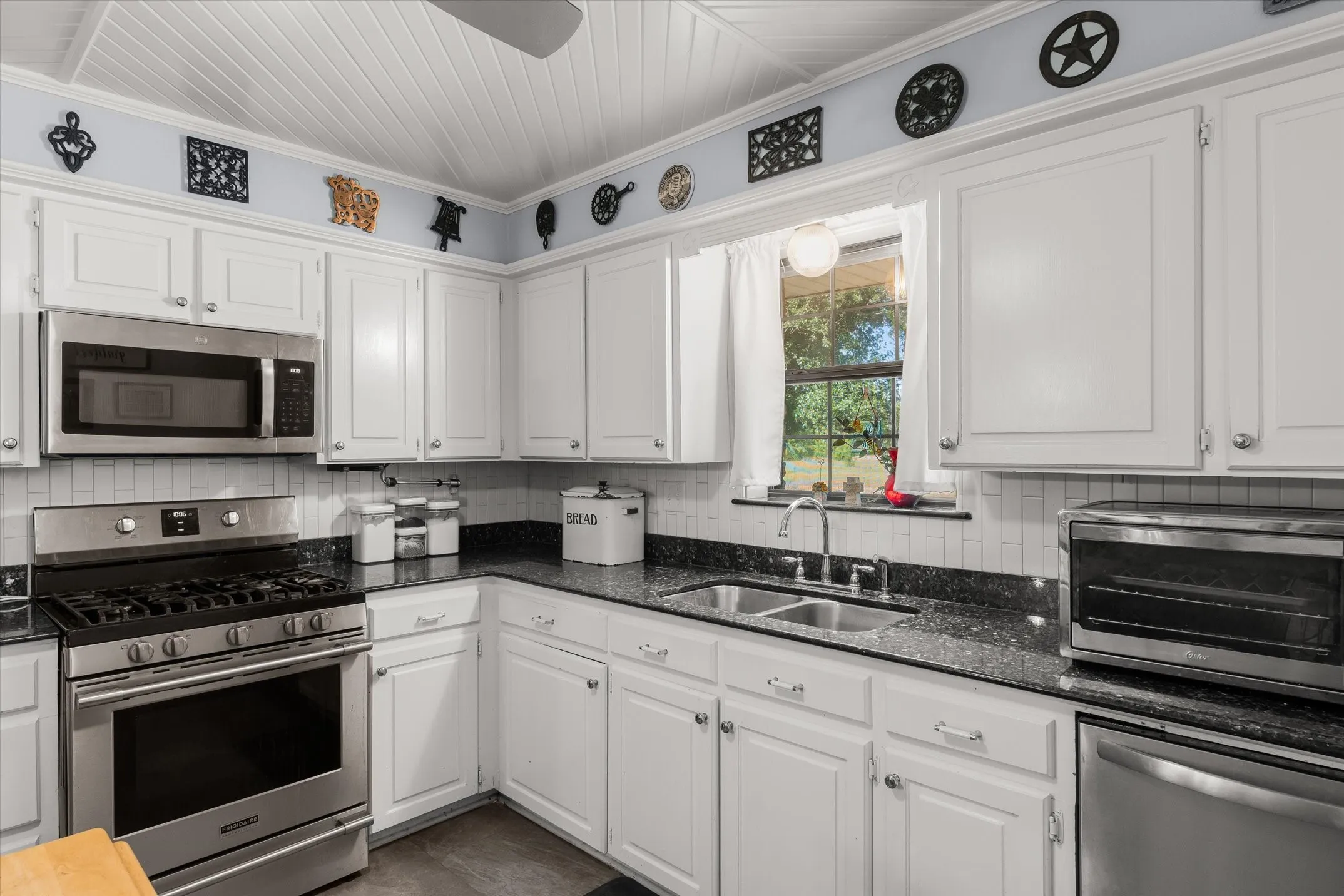 White cabinetry with silver hardware, dark countertops, white tile backsplash, and stainless steel appliances