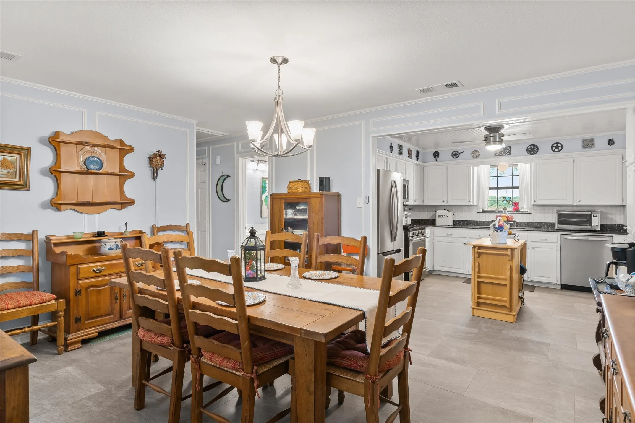 Open concept dining and kitchen area with light gray flooring, white cabinetry, dark countertops, and stainless steel appliances