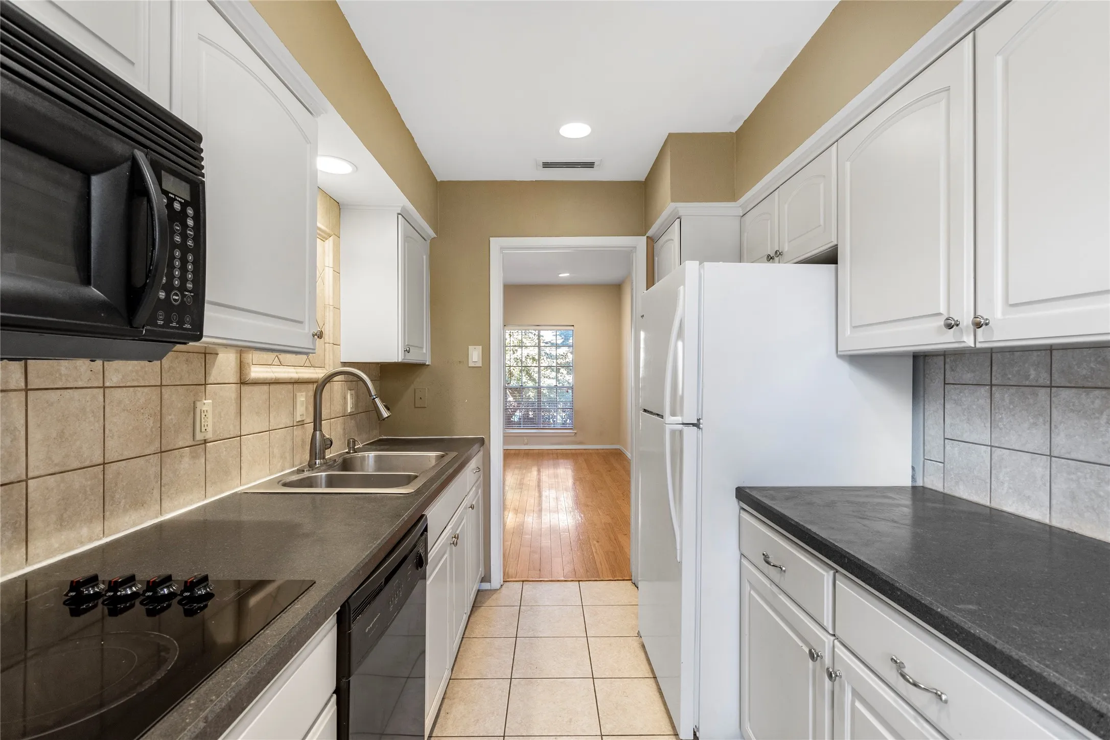 Kitchen with backsplash, black appliances, light tile patterned flooring, white cabinetry, and recessed lighting