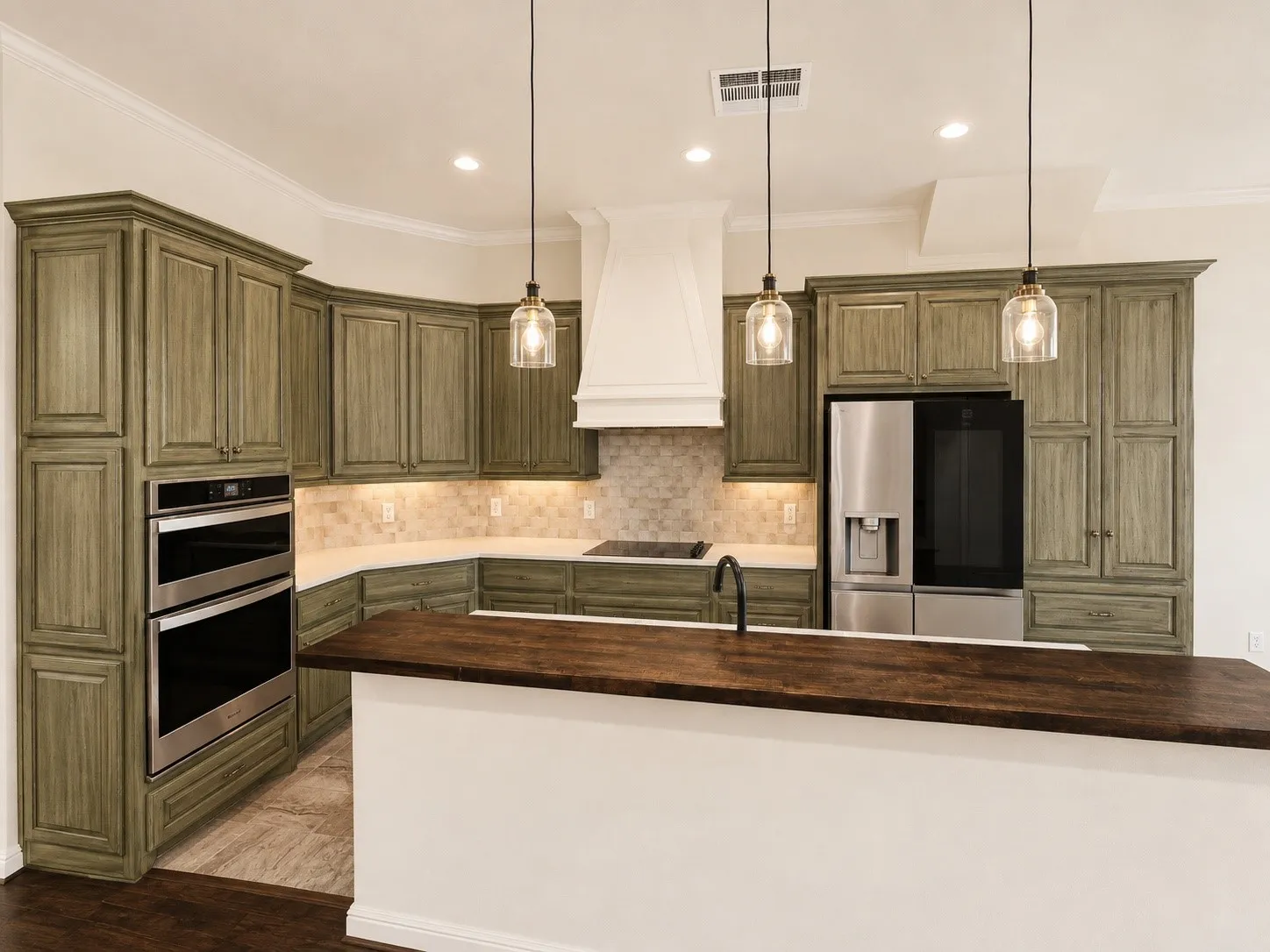 Kitchen featuring custom cabinetry, built-in double ovens, a stainless steel refrigerator, a large island with a wood-finish countertop, and pendant lighting