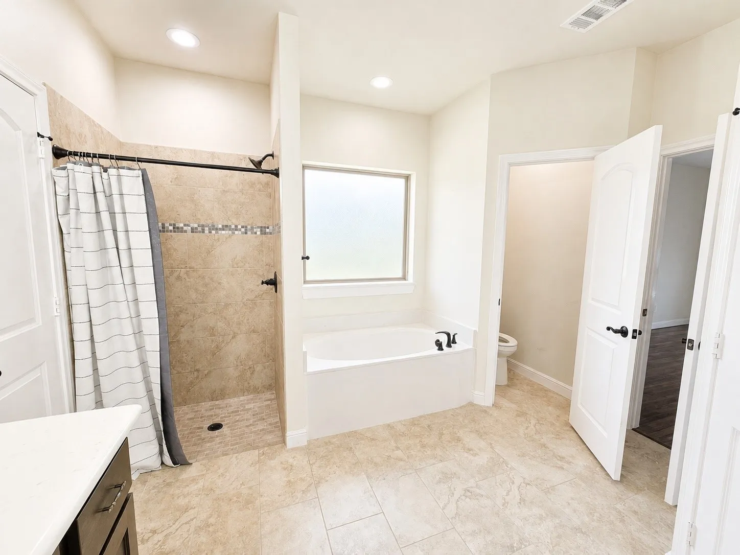 Tiled walk-in shower with decorative mosaic accent, garden tub with frosted window, and large format tiled flooring
