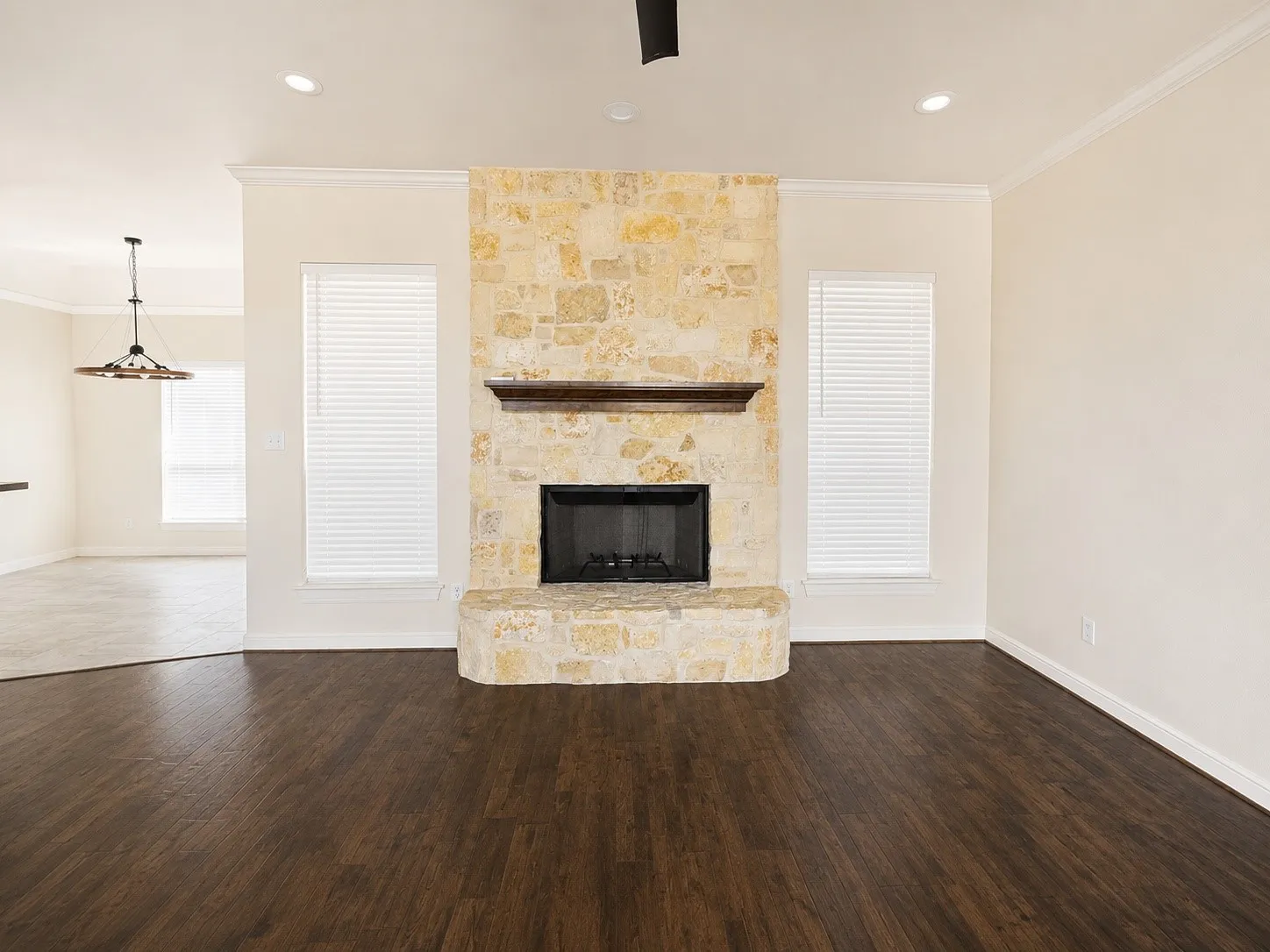 Stone-faced fireplace with a wood mantel, dark wood-finish flooring, recessed lighting, and crown molding