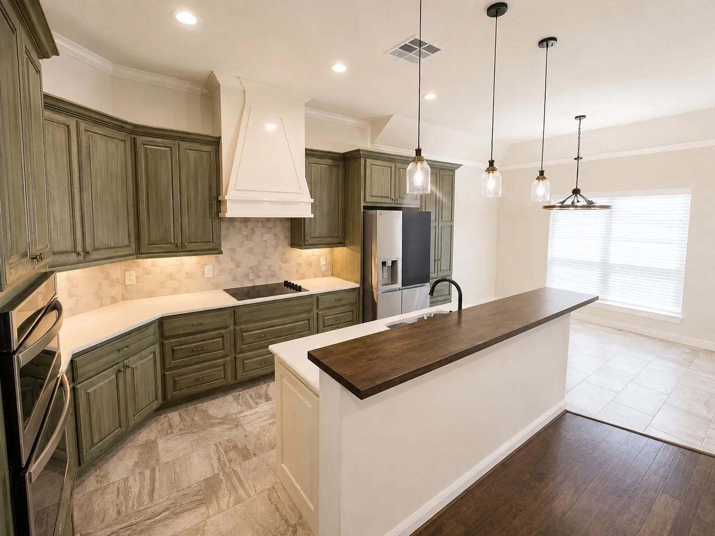 Kitchen featuring custom cabinetry, counter-depth refrigerator, built-in cooktop, and an island with a wood-finish counter