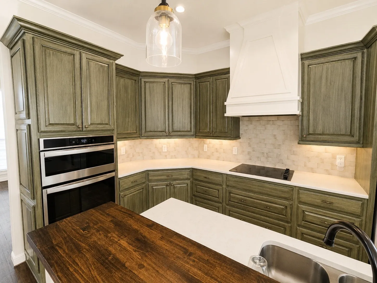 Kitchen featuring custom cabinetry, stainless steel double ovens, an integrated cooktop, a built-in range hood, and a dual-basin sink
