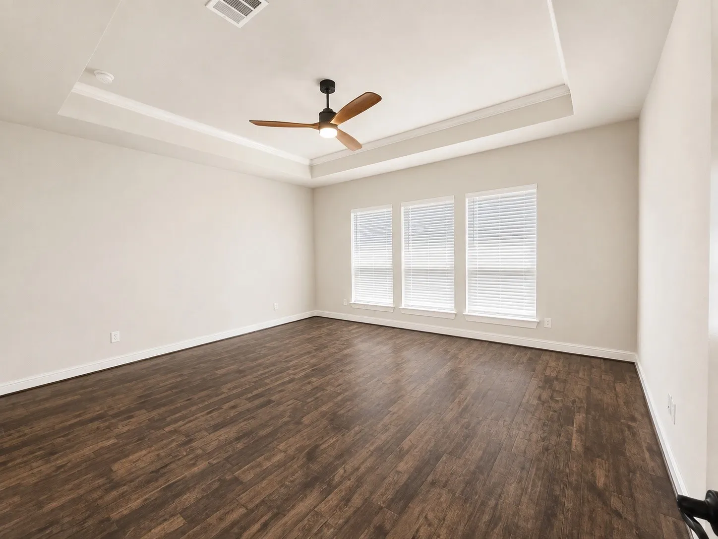 Tray ceiling with crown molding, wood-finish flooring, three windows with blinds, and a ceiling fan