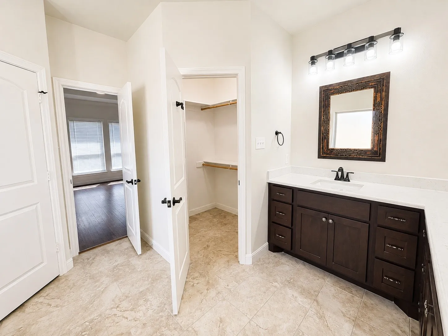 Spacious bathroom with light-toned tiled flooring, dark wood-finish vanity with ample storage, integrated sink, and white countertop