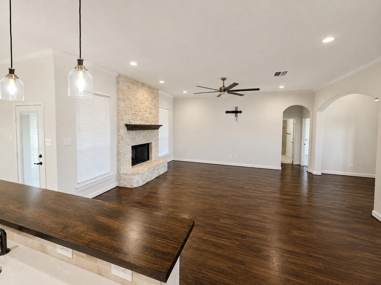 Stone-clad fireplace with a wood mantle, recessed lighting, wood-finish flooring, and a ceiling fan
