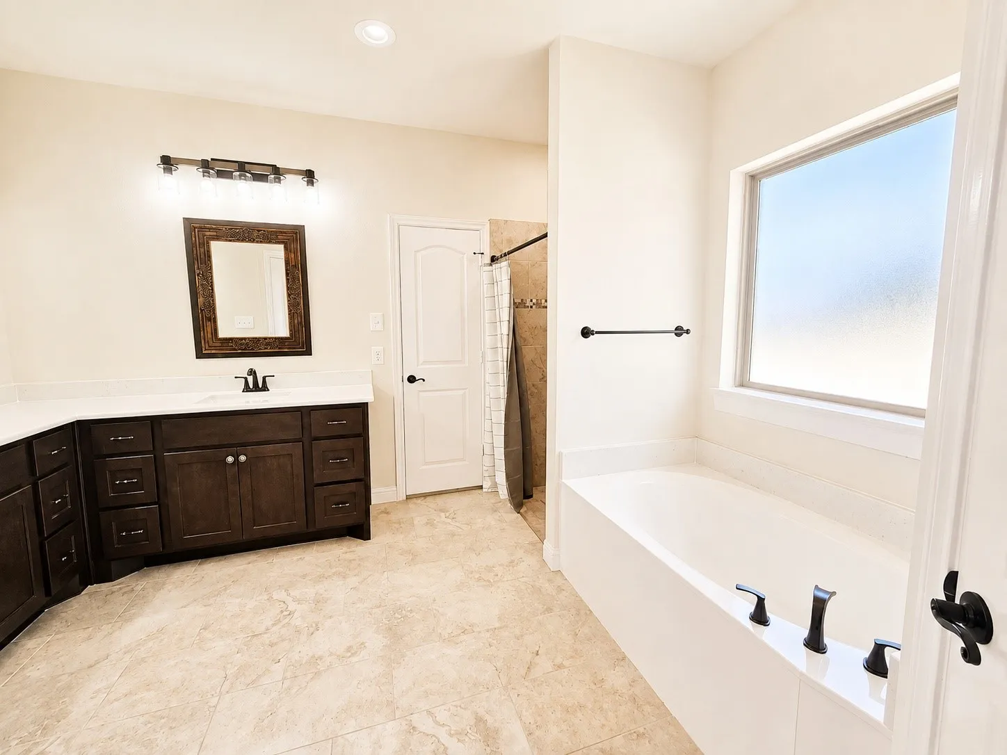 Built-in soaking tub with dark bronze fixtures, frosted window, dark wood vanity with white countertop, single basin sink, and tiled flooring