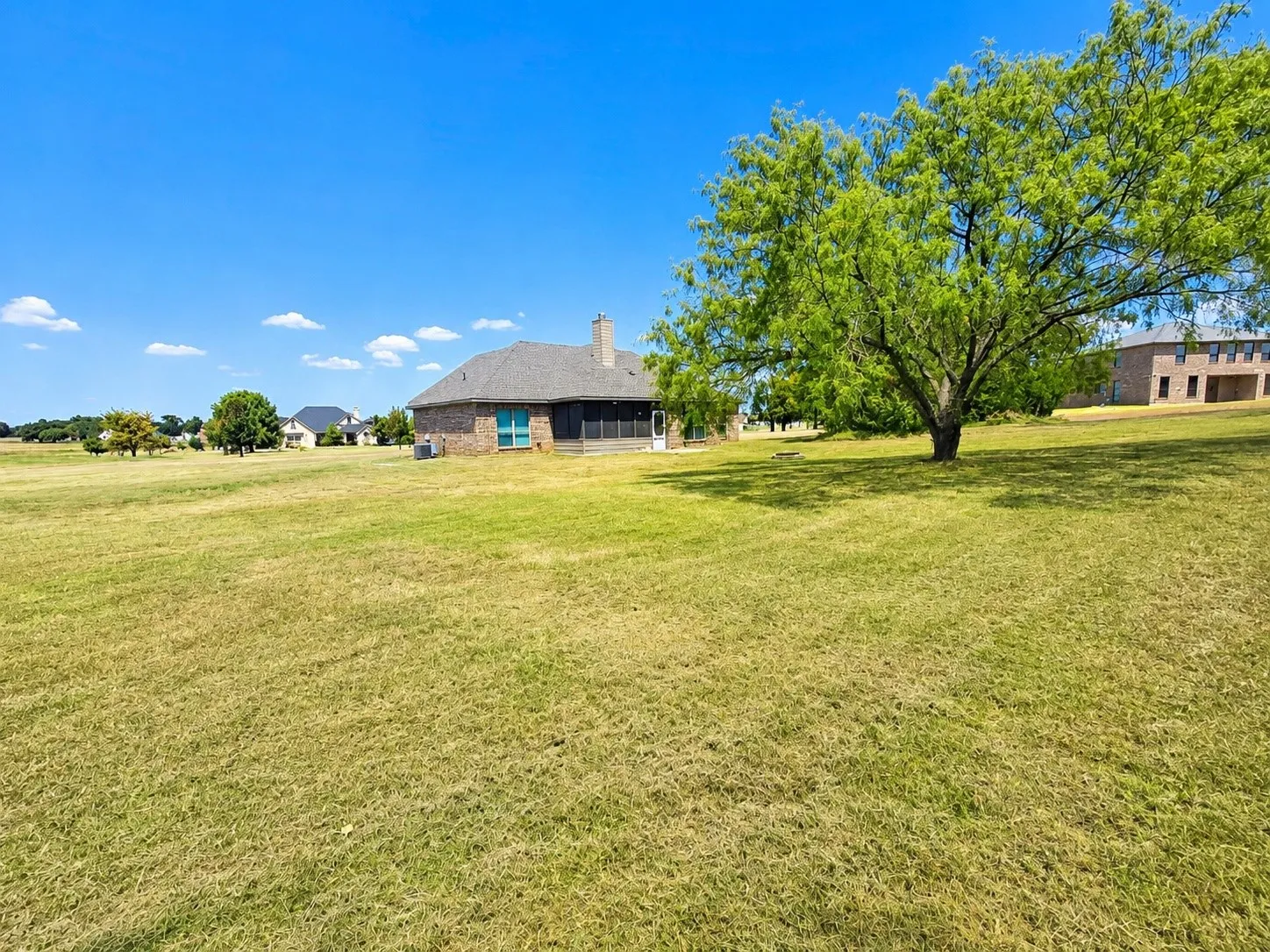Expansive lawn with a mature shade tree, brick exterior, and a screened outdoor living area