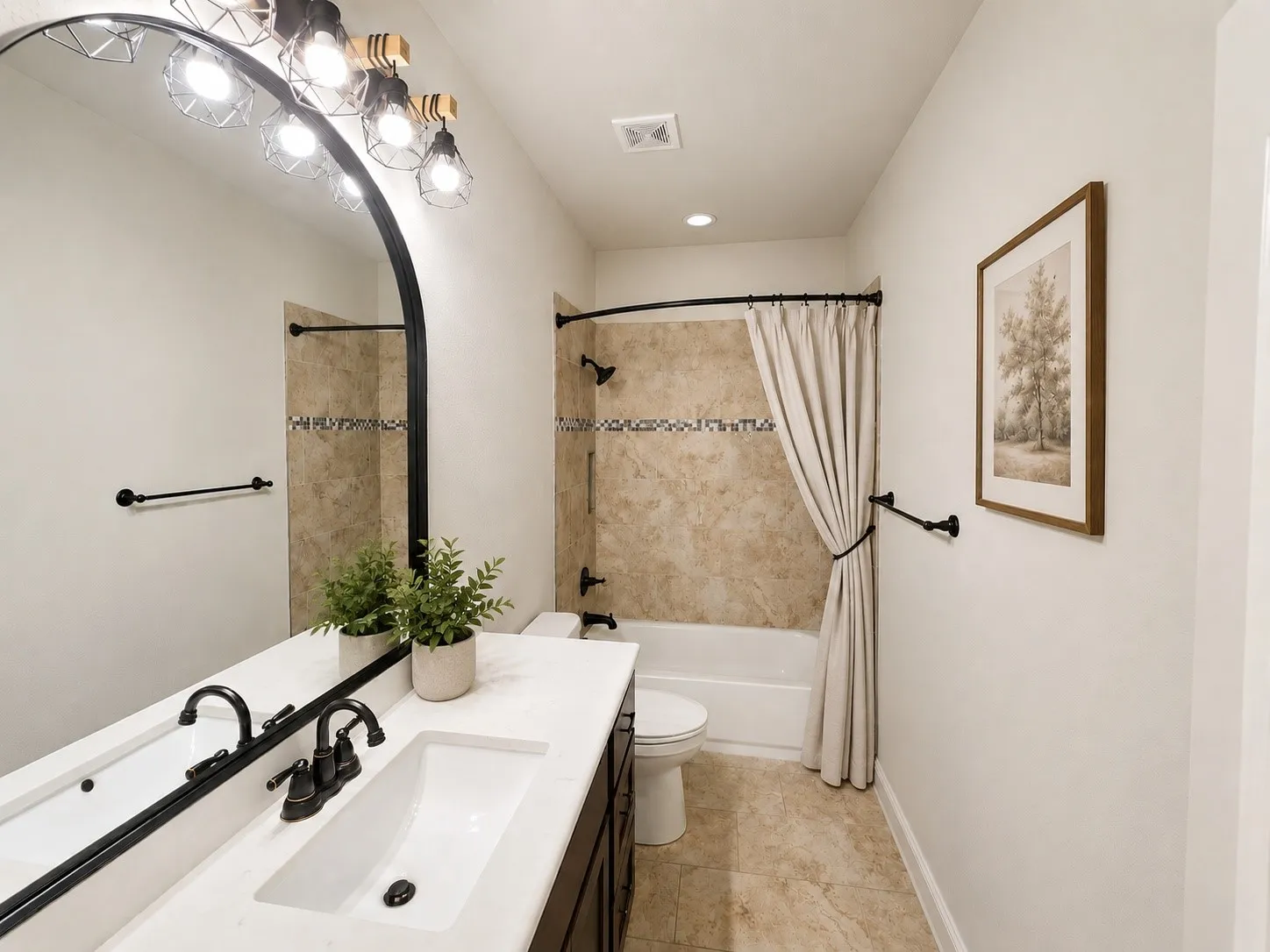 White countertop vanity with integrated sink and dark bronze faucet, arched mirror with industrial-style light fixture, and floor-to-ceiling tiled shower/tub combination