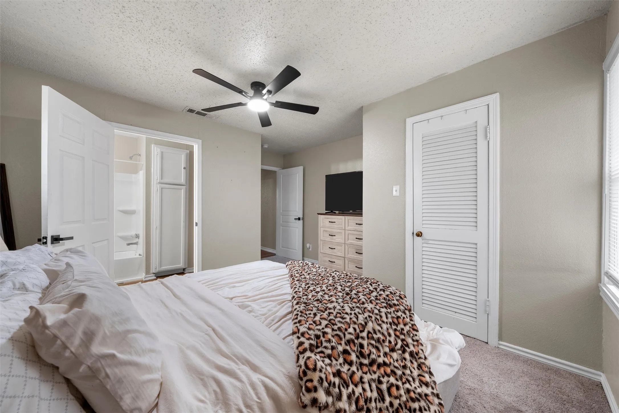 Neutral tone walls with textured ceiling, carpeted flooring, and a ceiling fan with integrated lighting