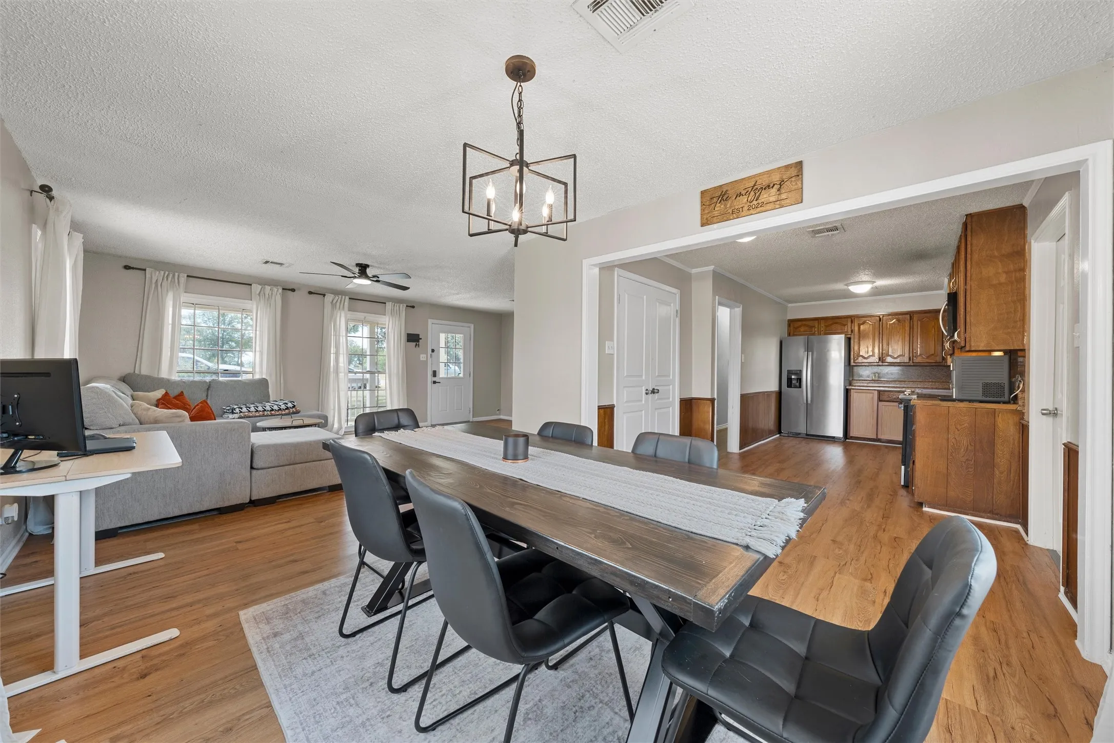 Wood-finish flooring throughout, with a square metal chandelier, and a ceiling fan in the living area