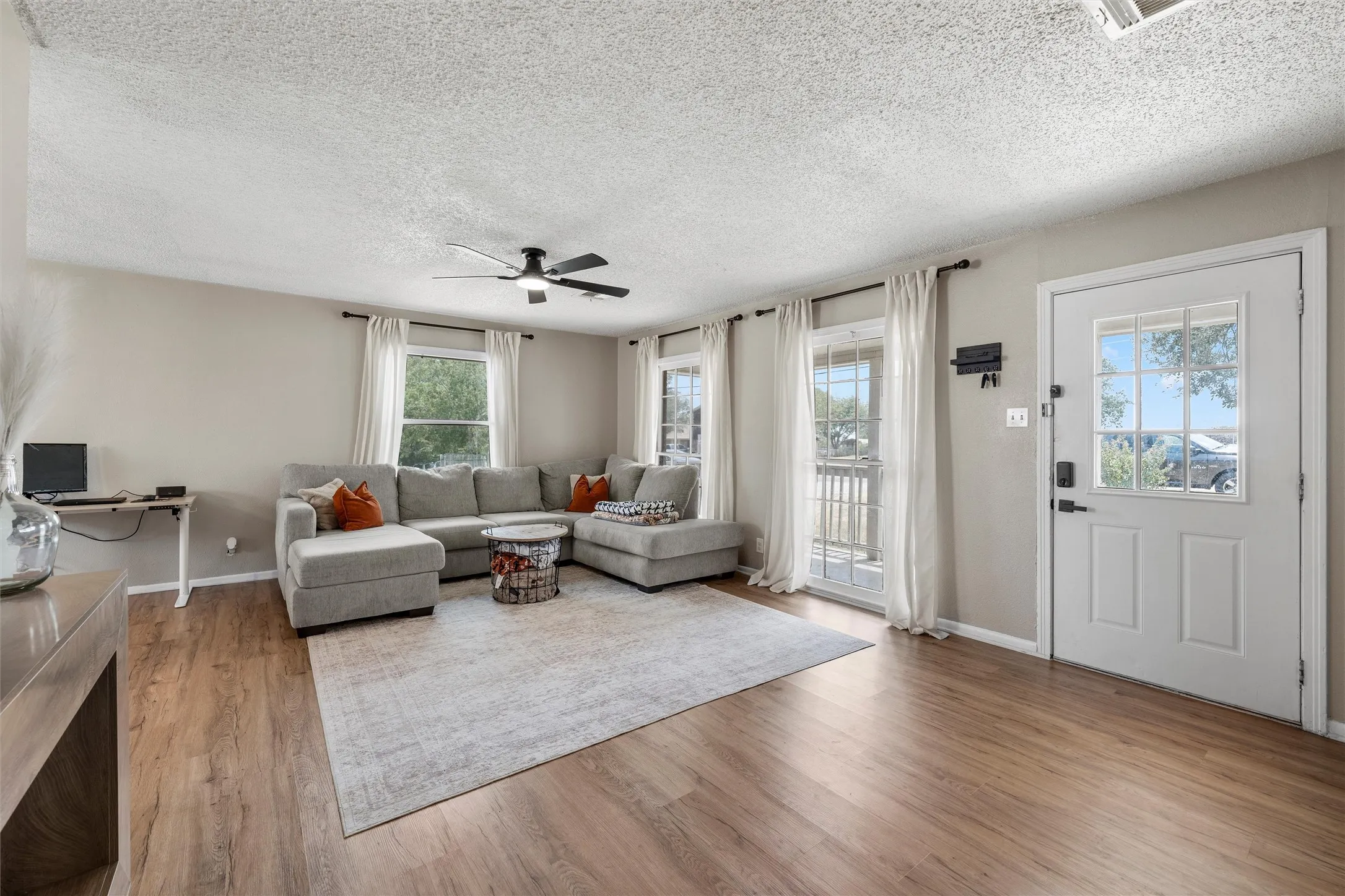 Wood-finish flooring throughout, multiple windows with natural light, ceiling fan with light fixture, and a paneled entry door with glass inserts
