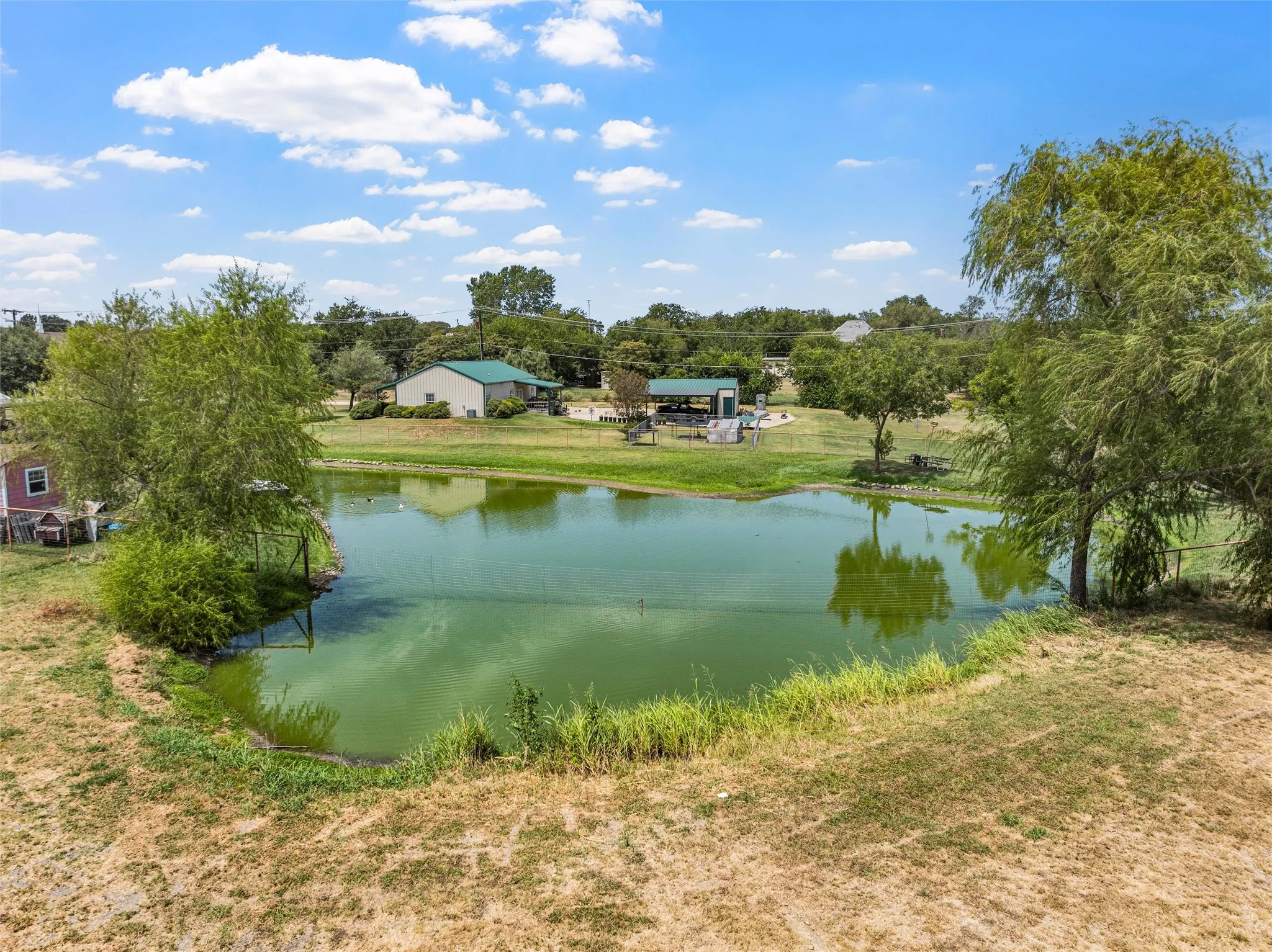 Expansive pond with surrounding mature trees, a green-roofed structure, and a covered outdoor area