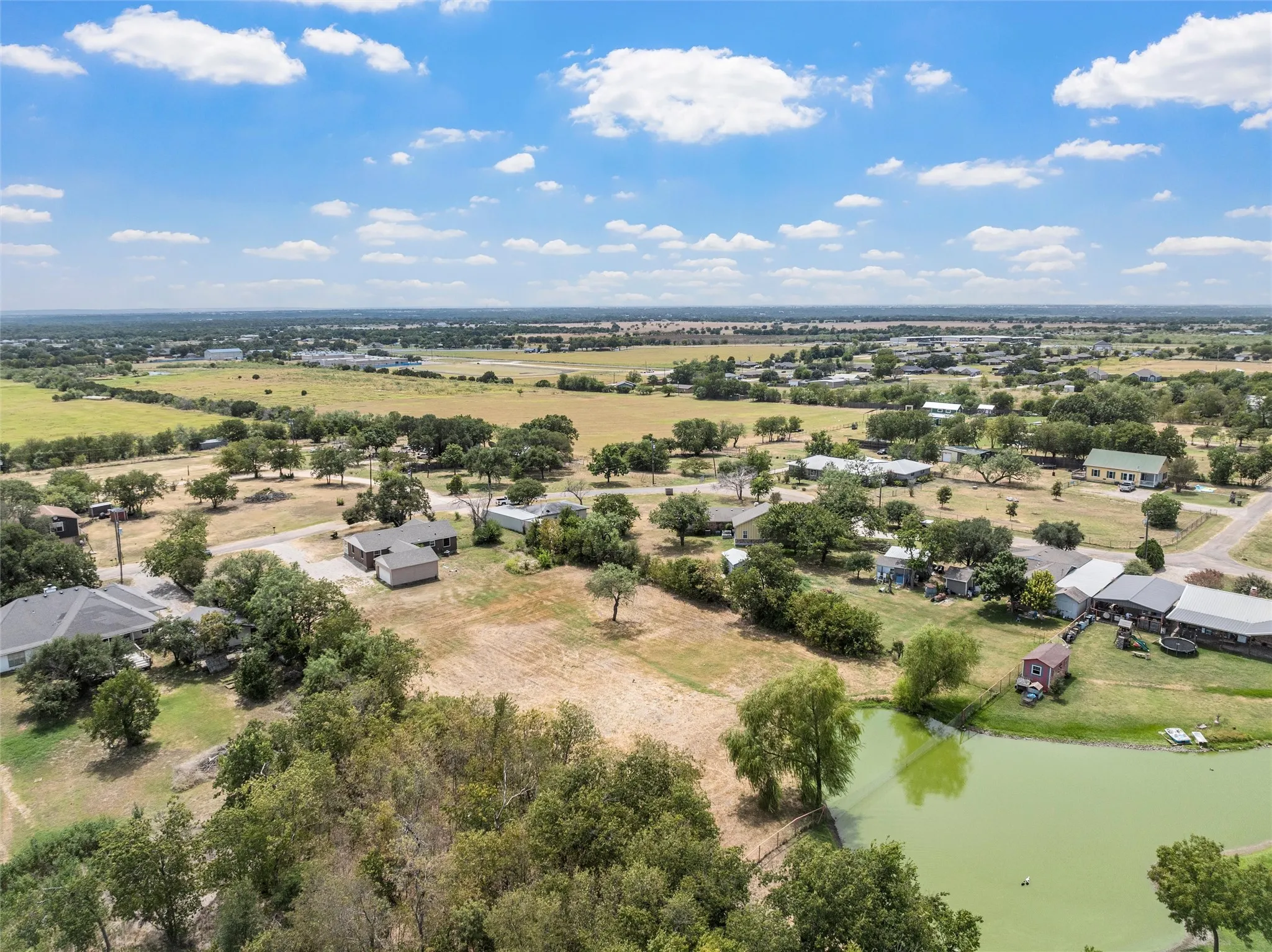 Expansive land with a pond and abundant trees, surrounded by open fields and additional residences