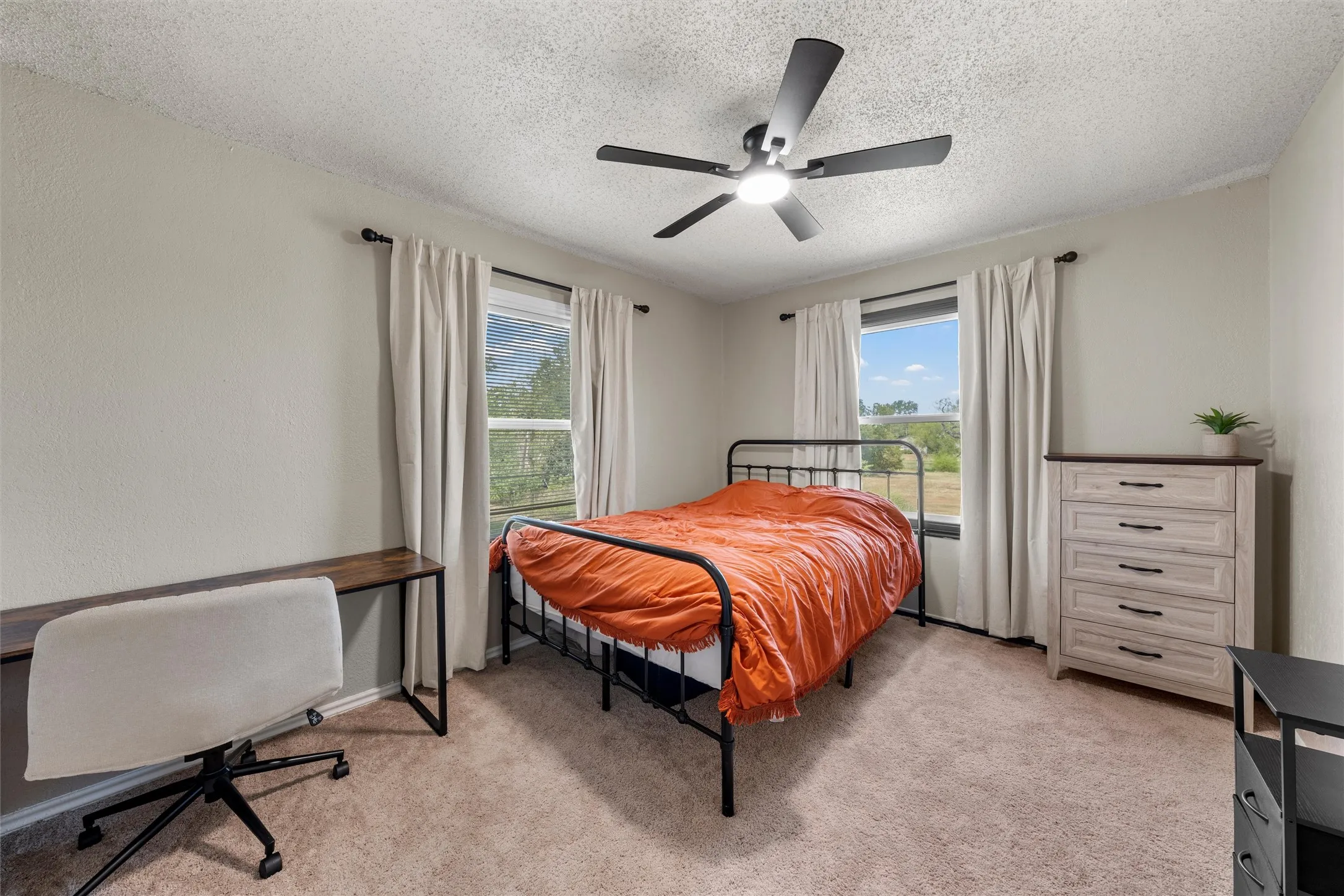 Textured wall finish, ceiling fan with integrated lighting, wood-finish desk, and window with outdoor scenery