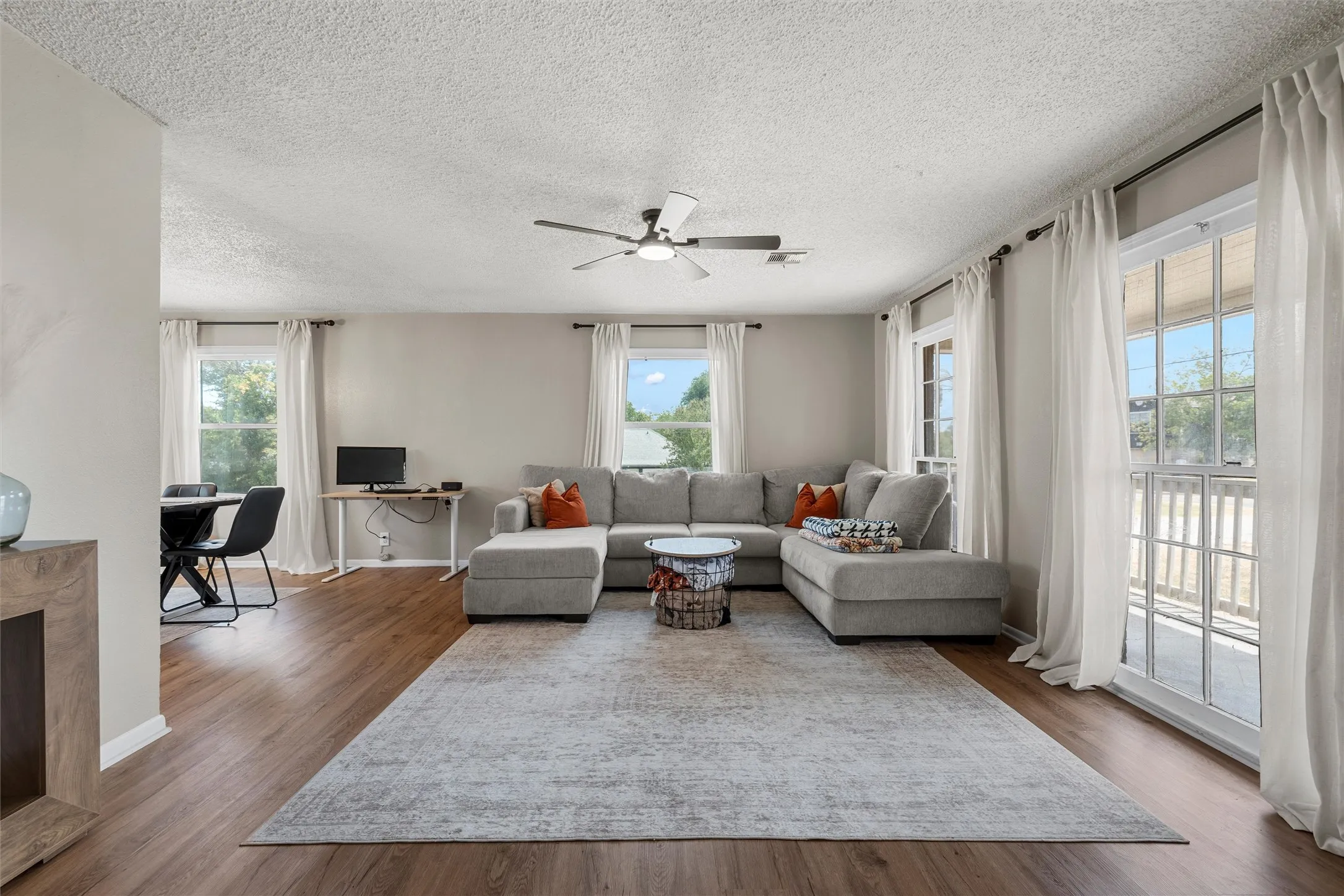Wood-finish flooring throughout, multiple large windows with white trim, and a ceiling fan with integrated lighting