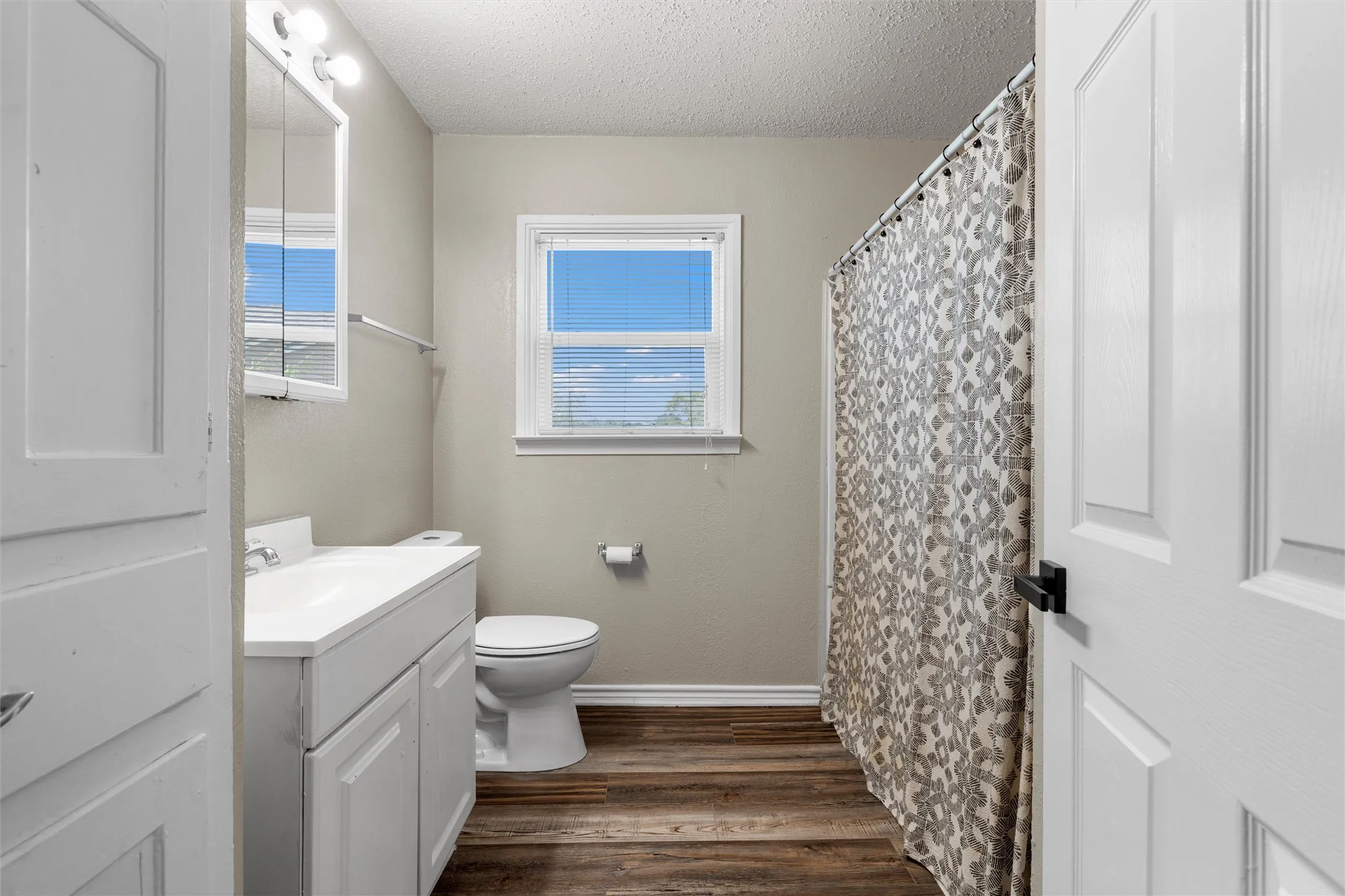 Bathroom featuring wood-finish flooring, a white vanity with integrated sink, and a framed mirror cabinet