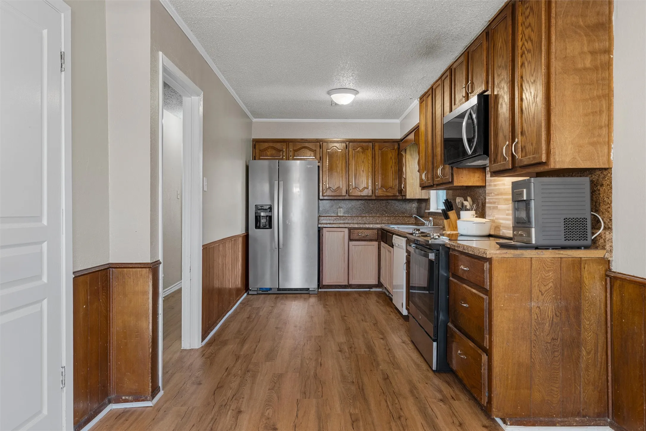 Kitchen featuring wood-finish flooring, wood cabinetry, stainless steel refrigerator, black and stainless steel microwave, and integrated dishwasher