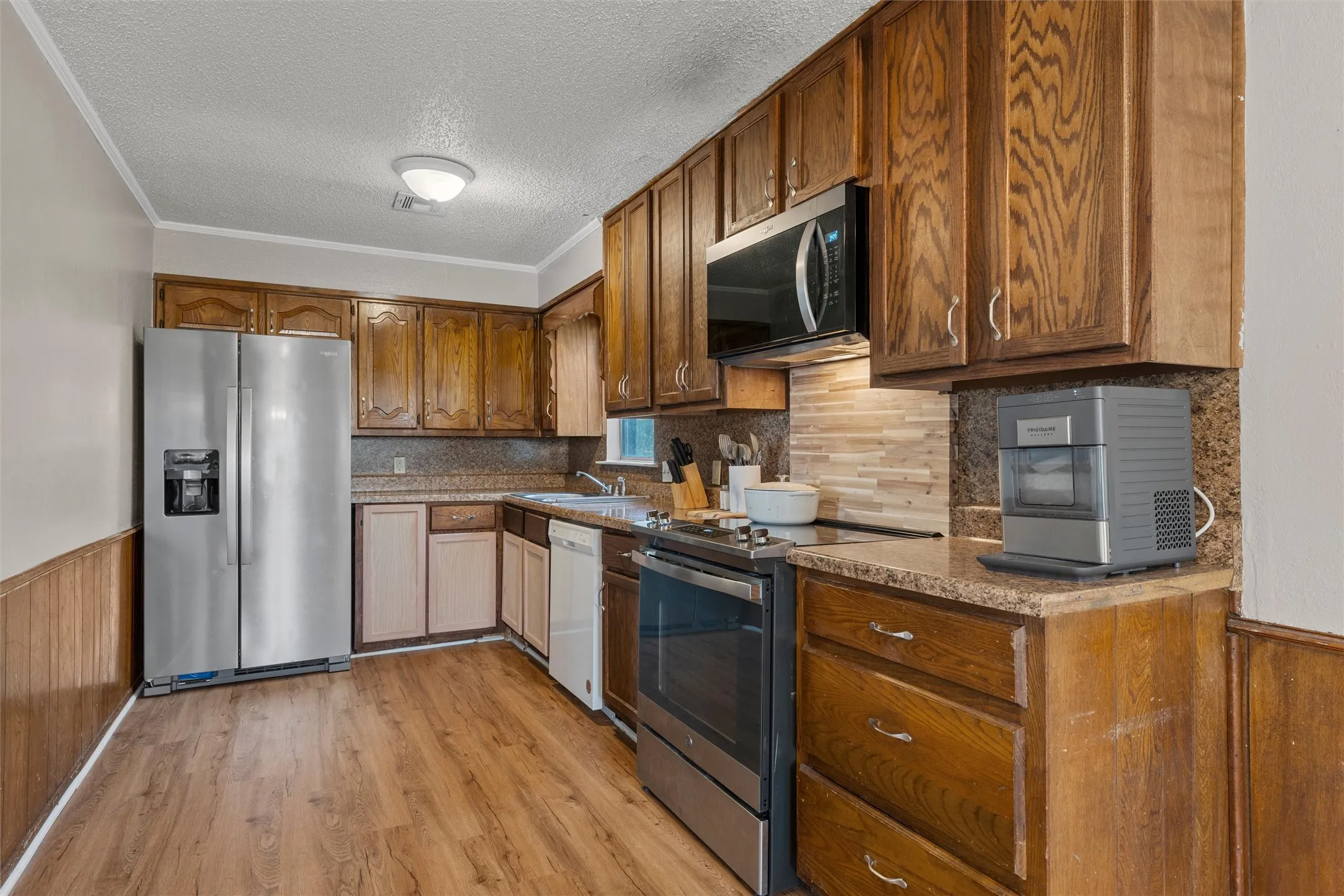 Wood-finish flooring, wood cabinetry, stone-finish countertops, stainless steel appliances, and a tile backsplash