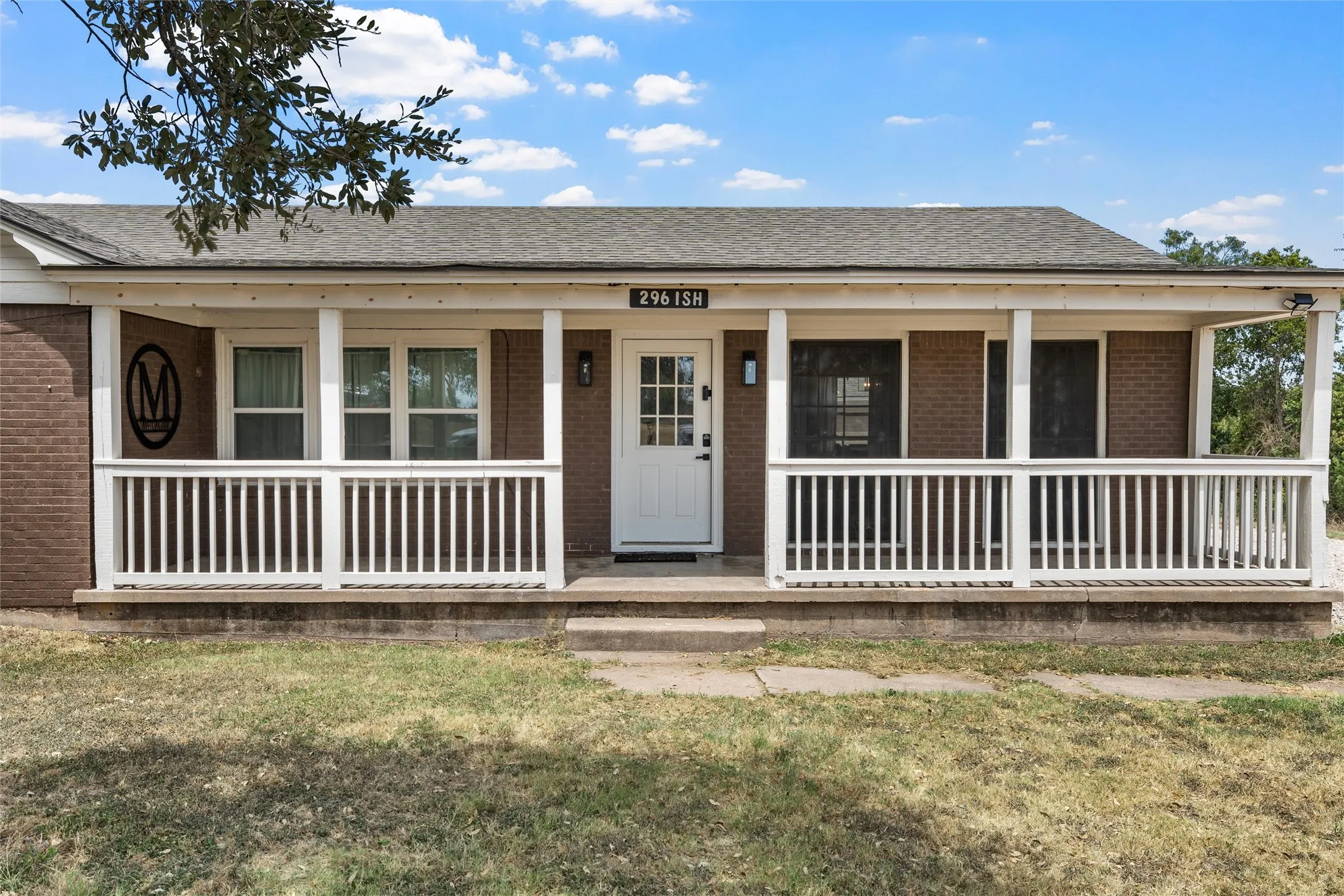 Brick exterior with a covered porch featuring white railings, a white entry door, and exterior lighting fixtures