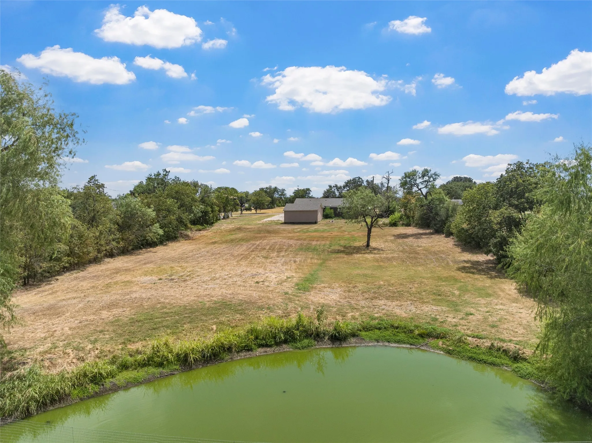 Expansive land parcel featuring a private pond, mature trees, and a distant structure