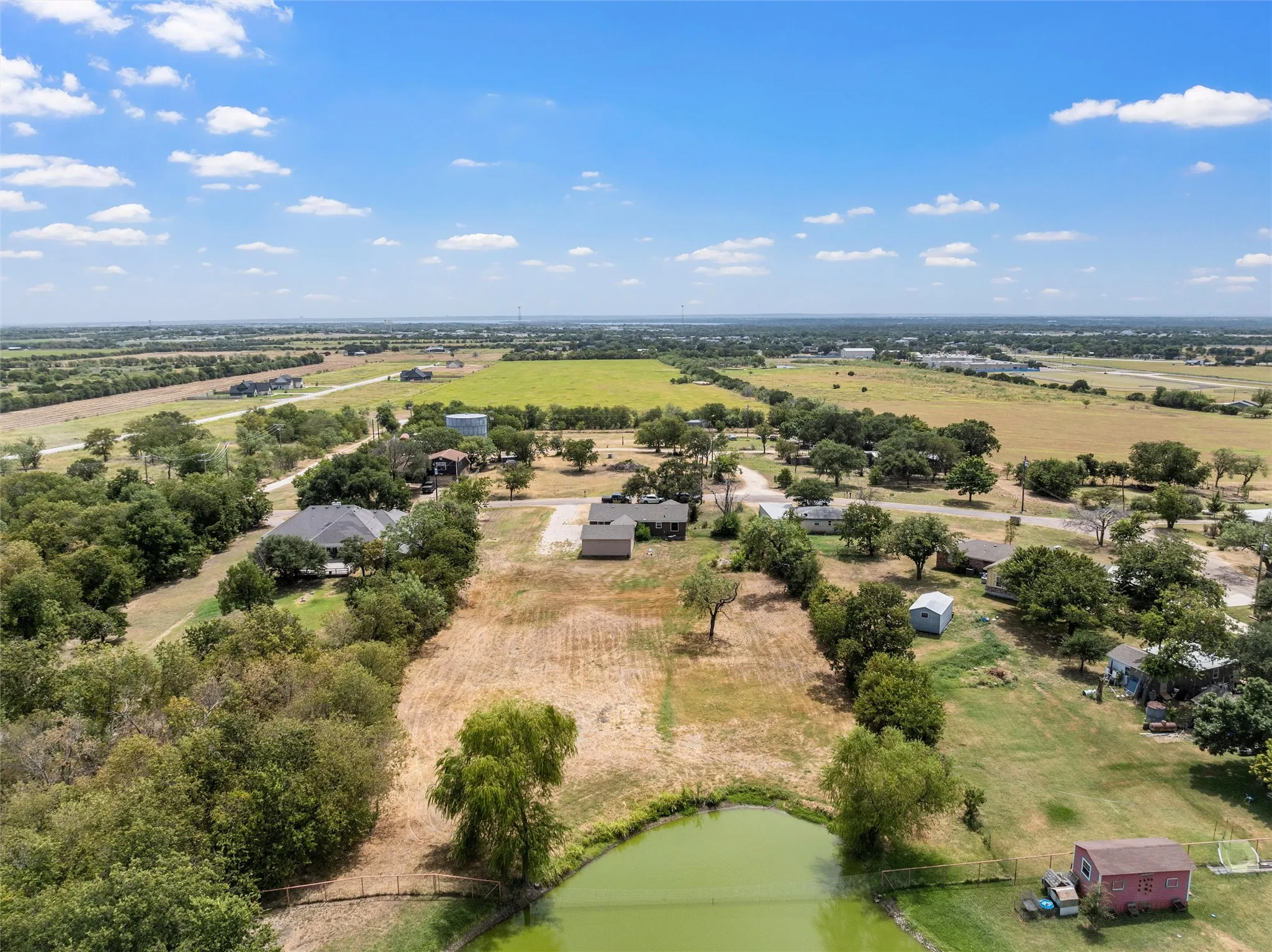 Expansive acreage featuring a pond, established trees, and surrounding open fields