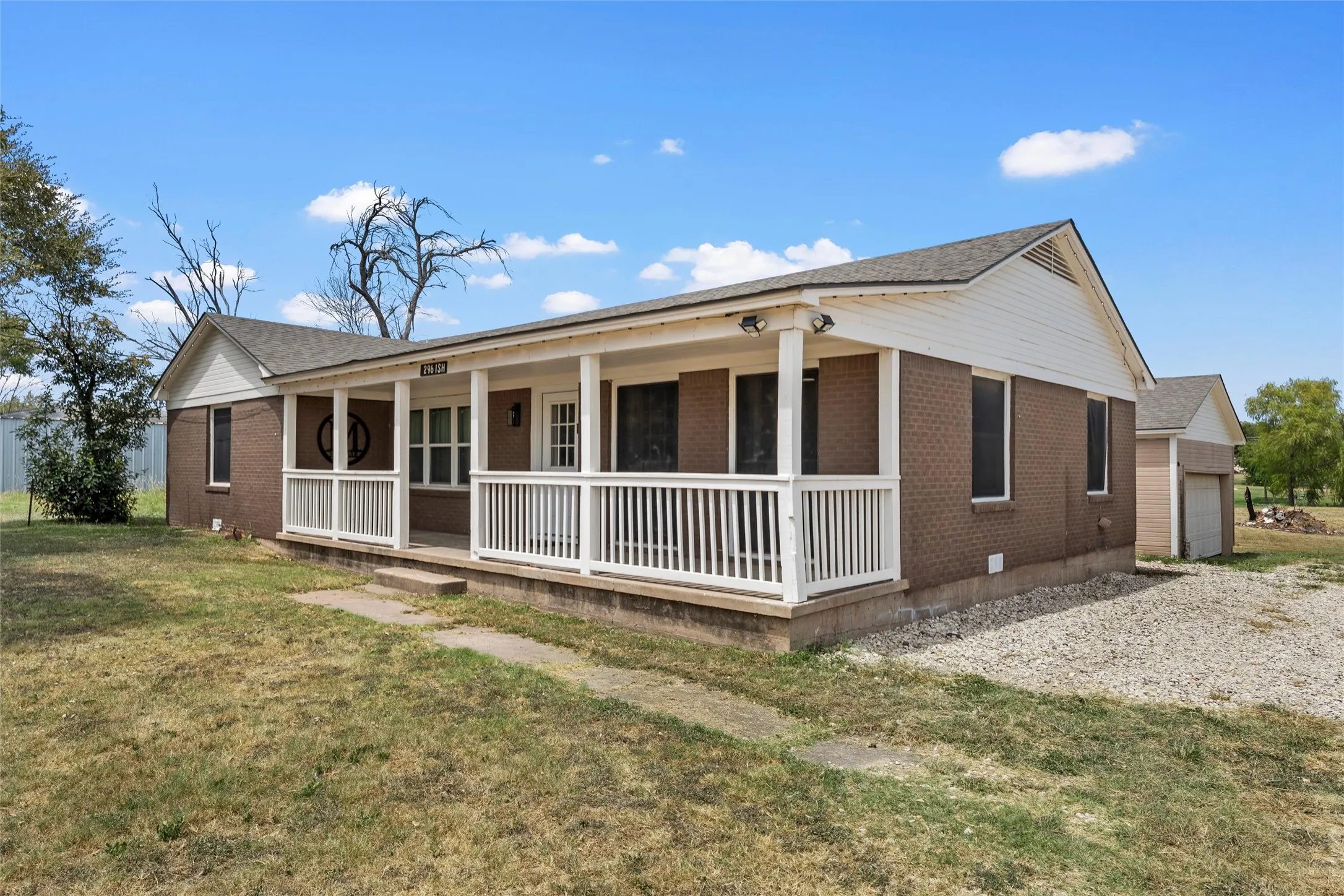 Brick exterior with white trim, covered front porch, white porch railing, and a detached garage structure