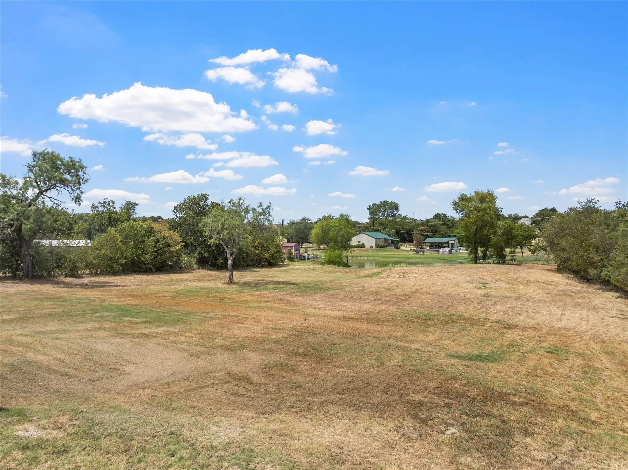Expansive open field with scattered trees and distant structures