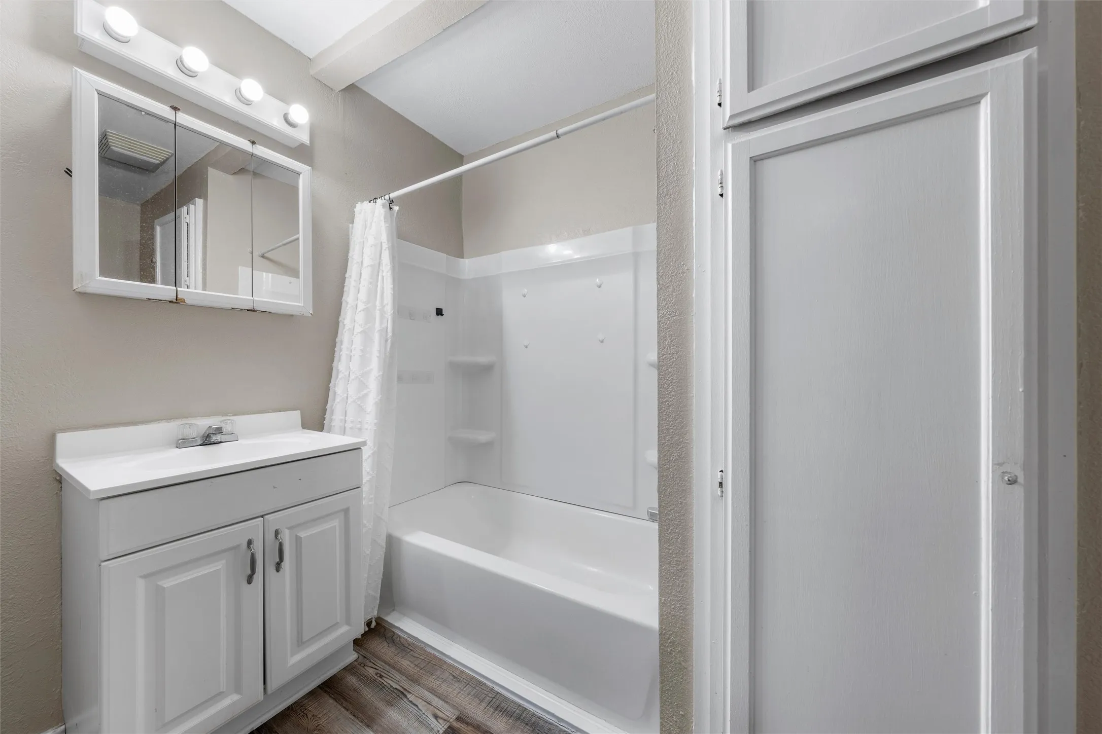 White vanity with a single basin sink, medicine cabinet with integrated lighting, and a white tub with shower