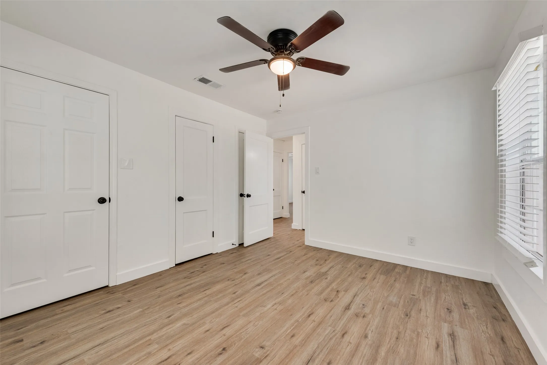 Wood-finish flooring, white paneled doors, ceiling fan with integrated lighting, and window with blinds
